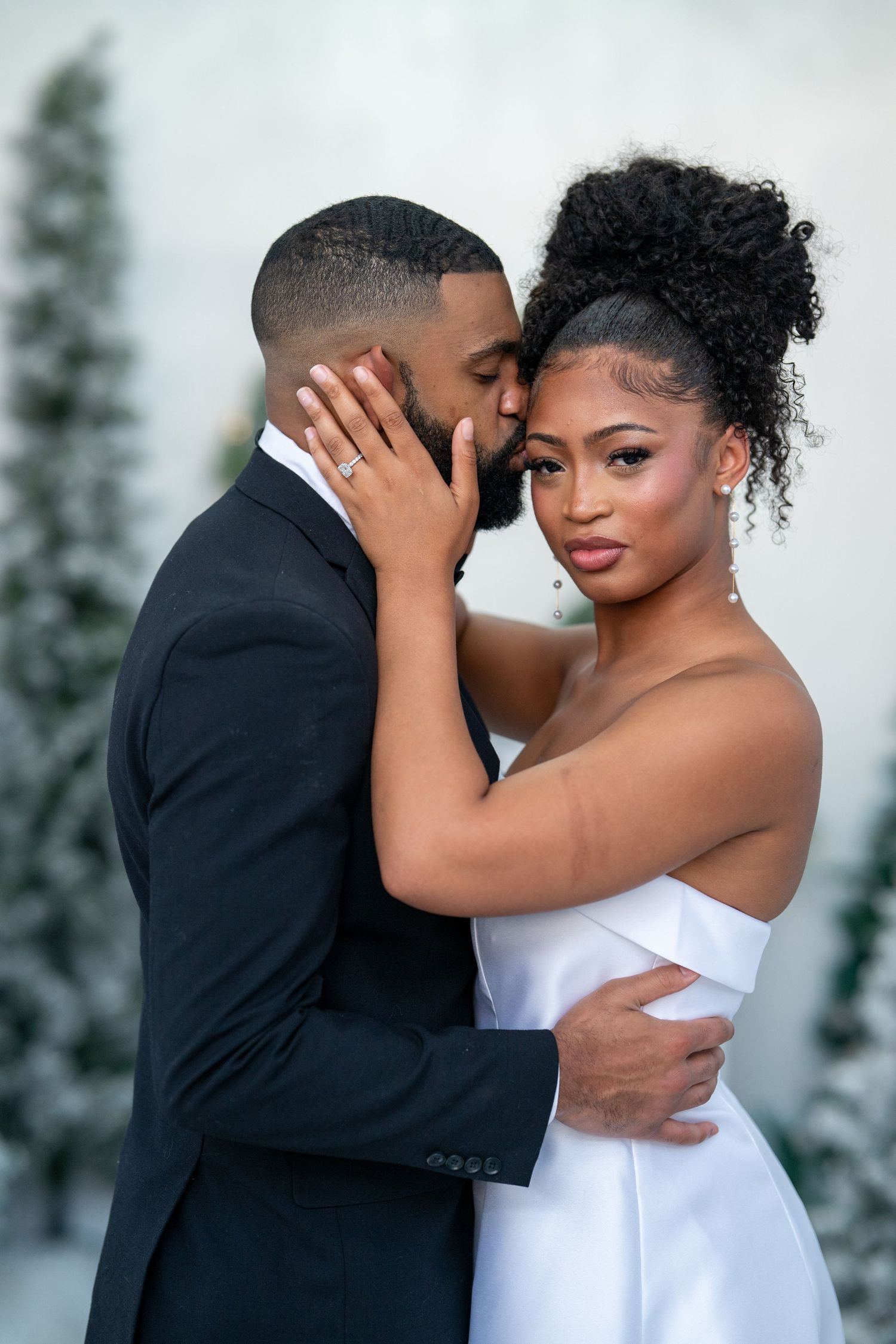 Elegant Black couple in wedding attire embracing tenderly in front of snowy pine tree backdrop.