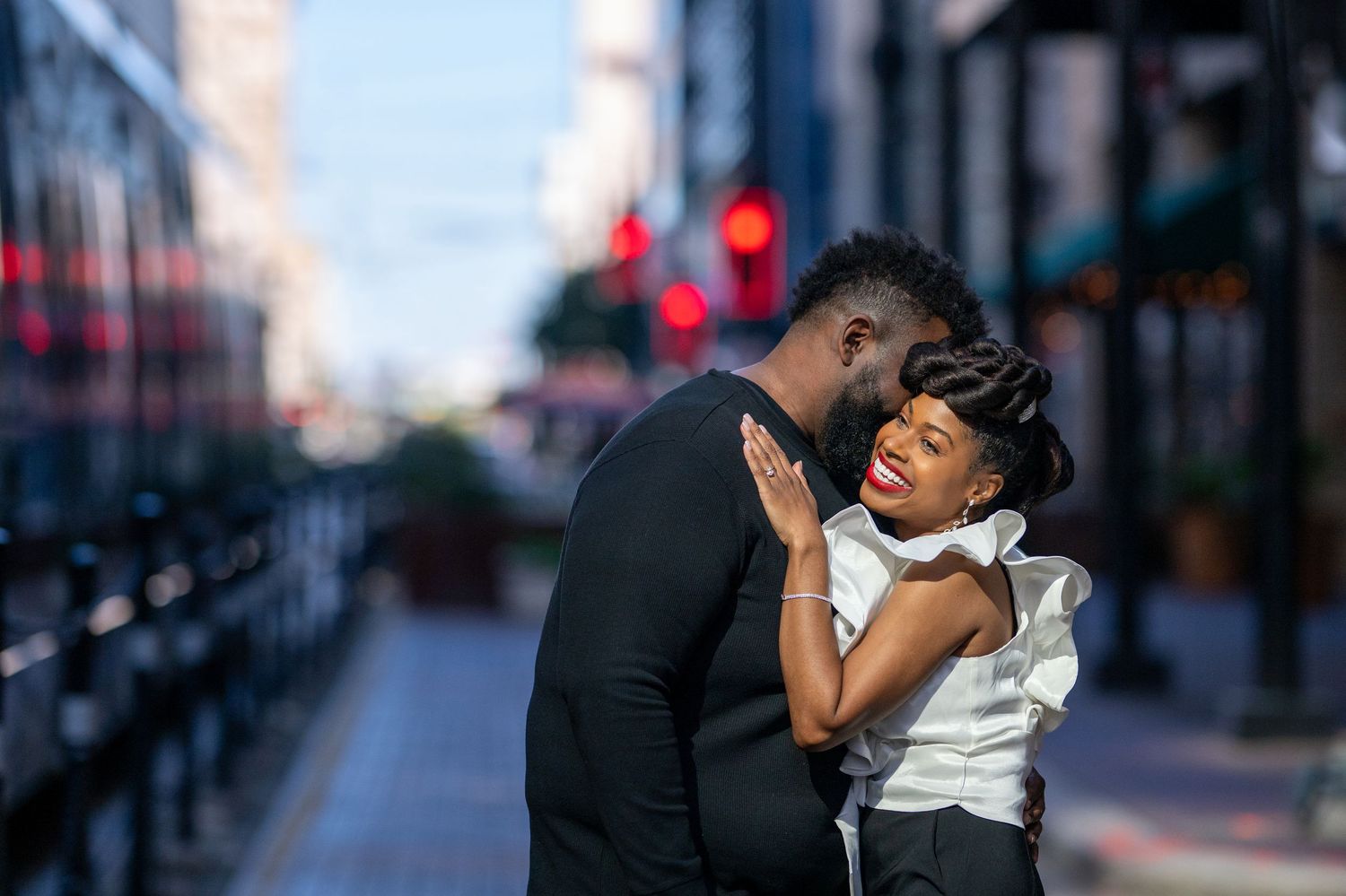 A couple shares a romantic moment on a city street, with the man leaning in to kiss the woman's cheek.