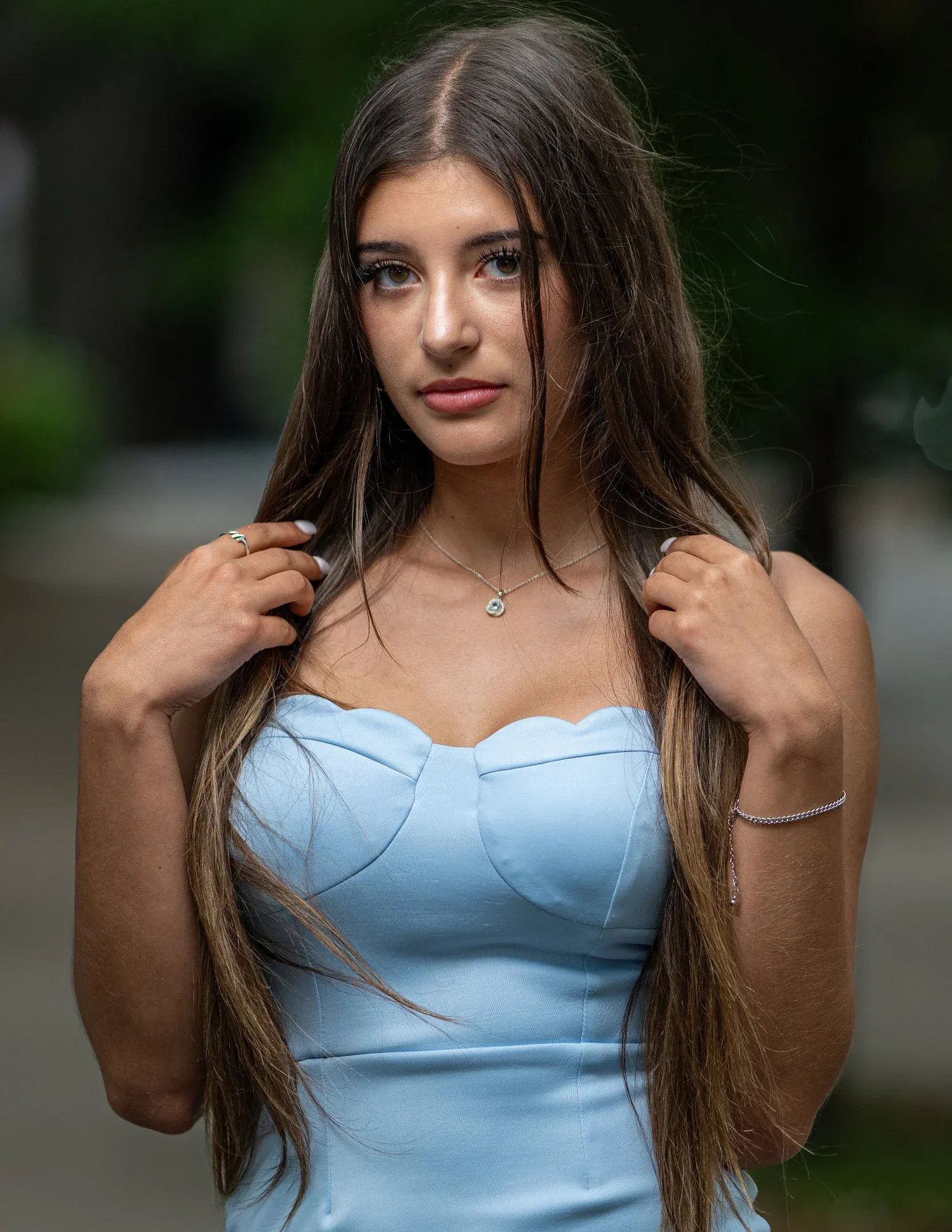 Young woman with long dark hair in a light blue strapless dress posing outdoors.