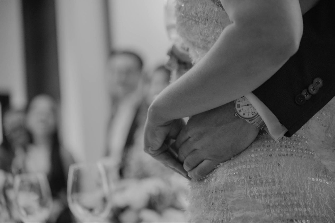 Black and white close-up of bride and groom holding hands during wedding reception.