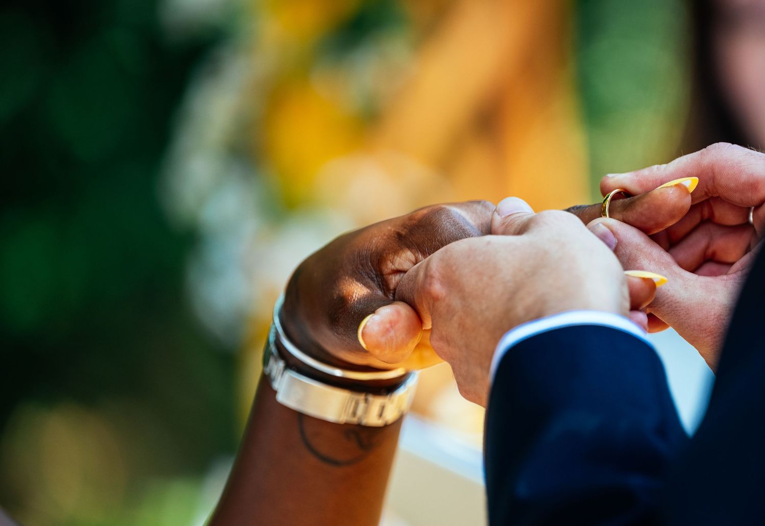 Close-up of a groom placing a gold wedding ring on the bride's finger during an outdoor wedding ceremony.