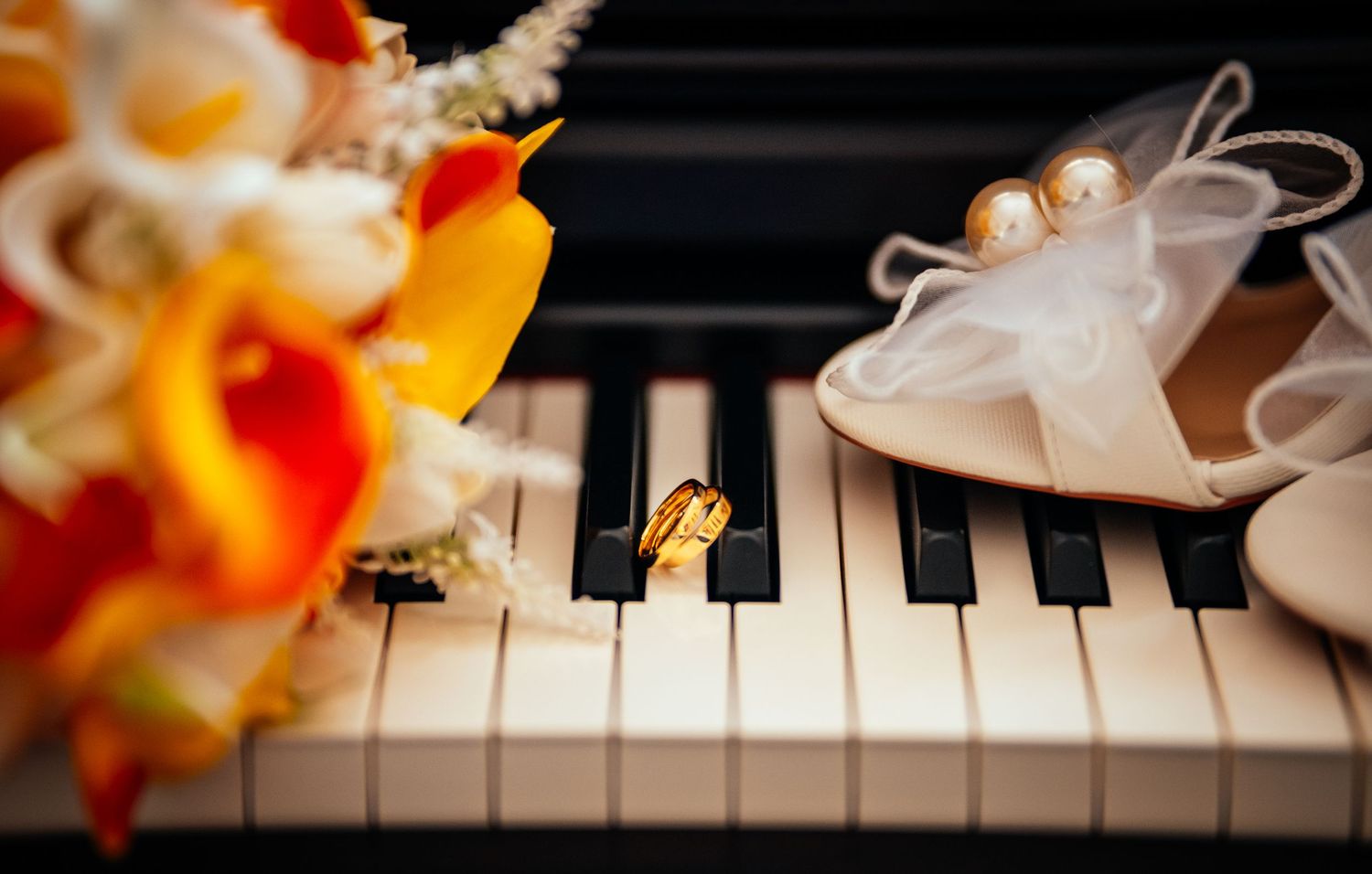Wedding rings, bridal bouquet, and pearl heels arranged on piano keys for an elegant wedding detail shot.