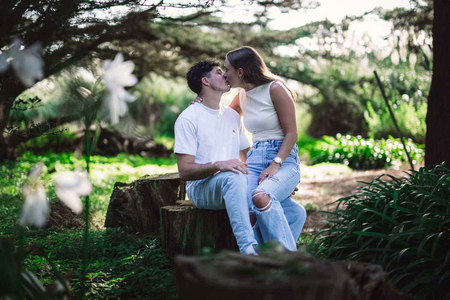 Romantic couple sharing a kiss while sitting on a tree stump in a lush garden.