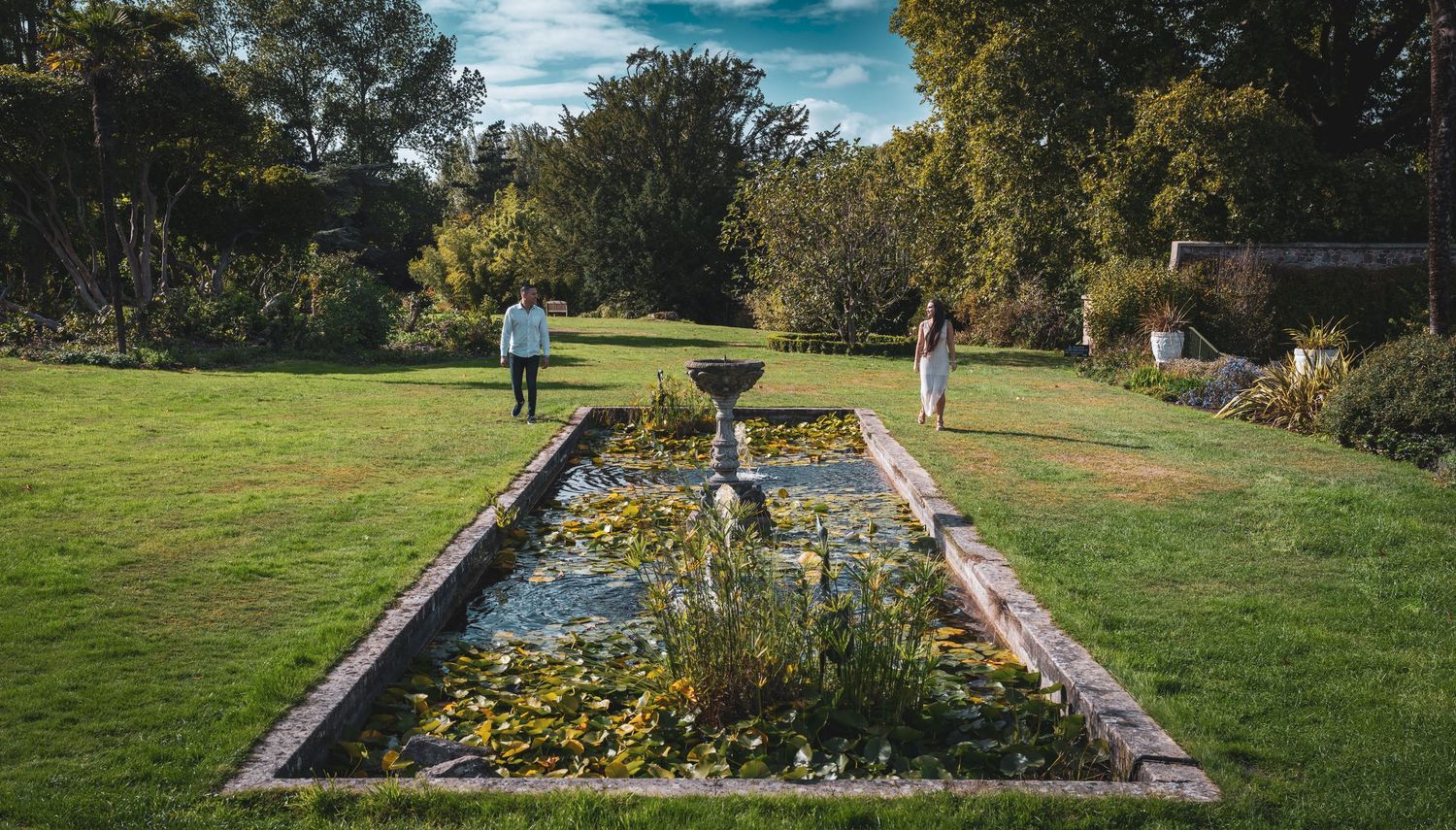 Couple walking toward each other beside a lily pond in a serene formal garden landscape.