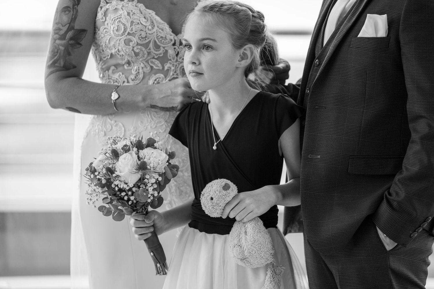 Black and white photo of young flower girl holding bouquet standing between bride and groom.