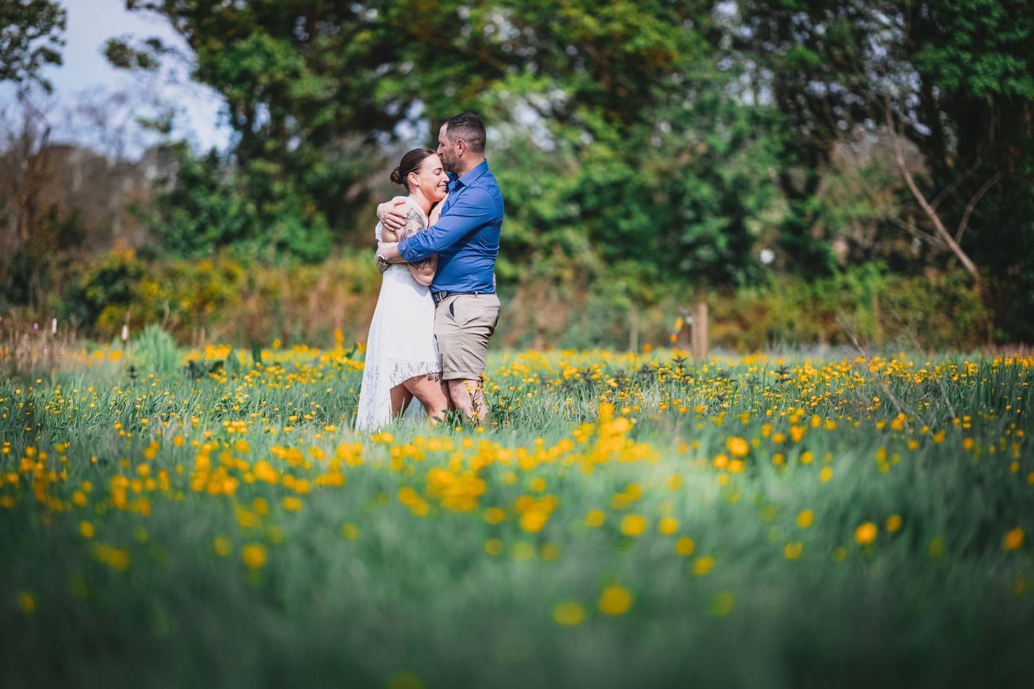 Couple embraces romantically in a vibrant field of yellow wildflowers outdoors.
