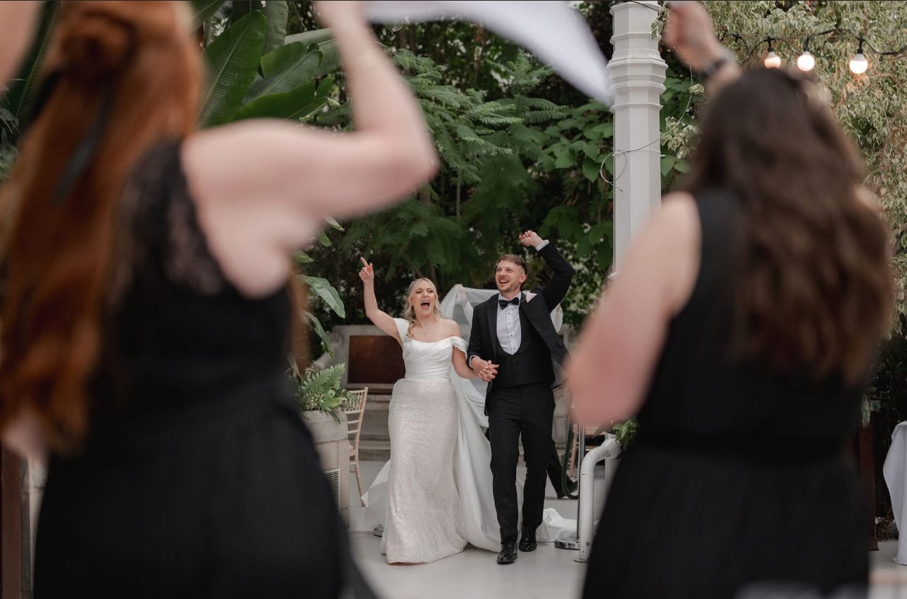 Joyful newlyweds walk through cheering guests at outdoor wedding reception celebration.