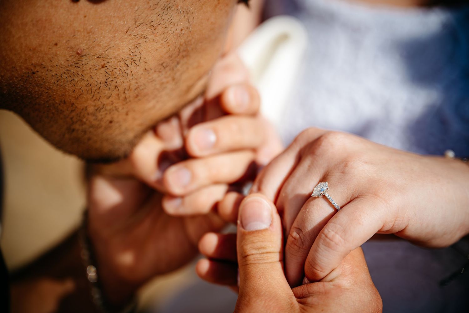 Groom tenderly kisses bride's hand adorned with sparkling diamond engagement ring closeup.