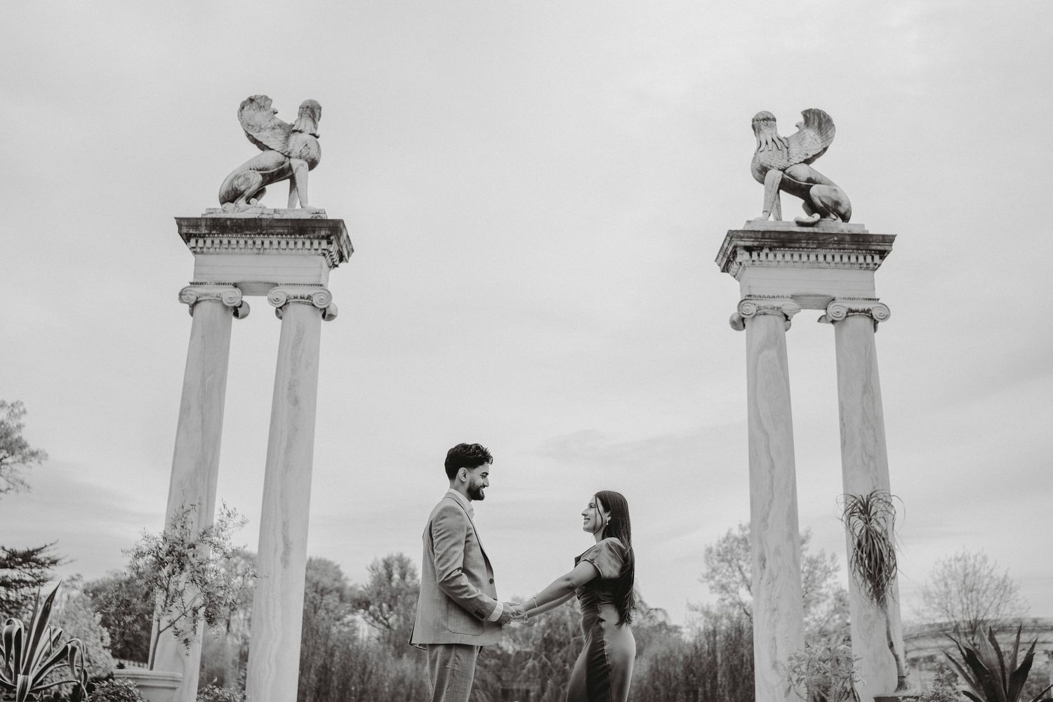 Black and white photo of couple facing each other between two tall columns with griffin statues.
