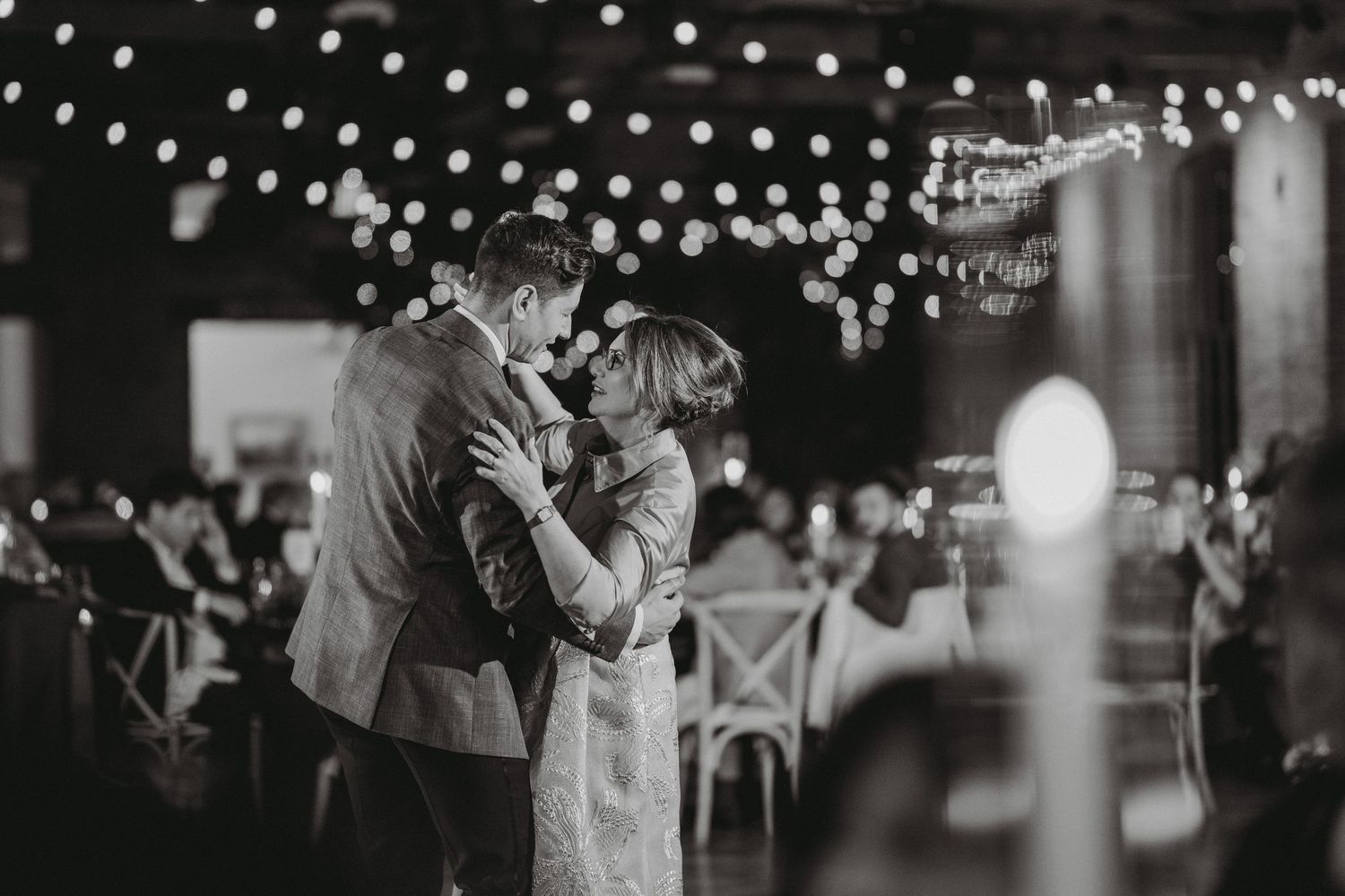 Couple shares intimate first dance under string lights at wedding reception.