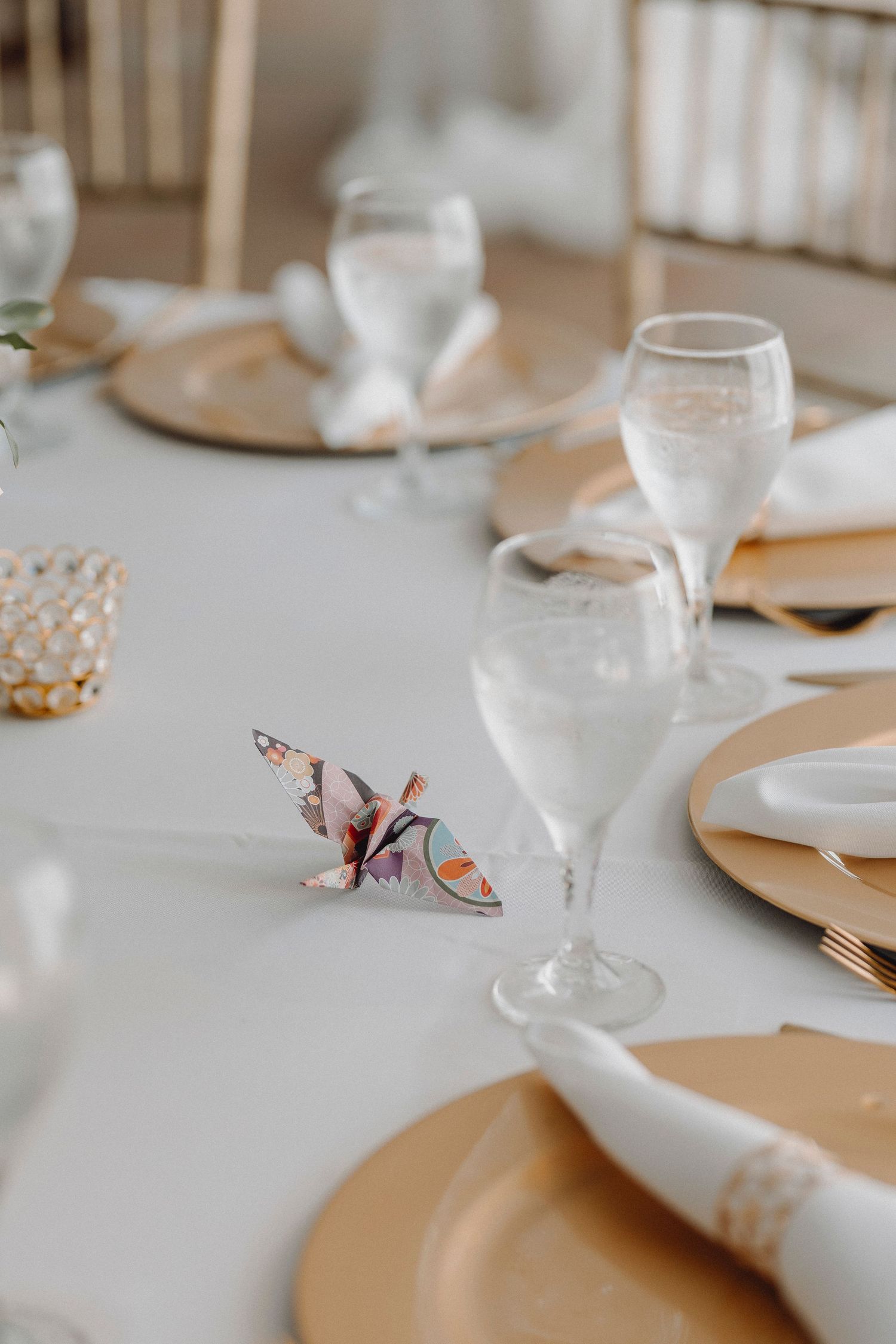 Elegant wedding table setting with gold charger plates, crystal glasses, and decorative origami butterfly.