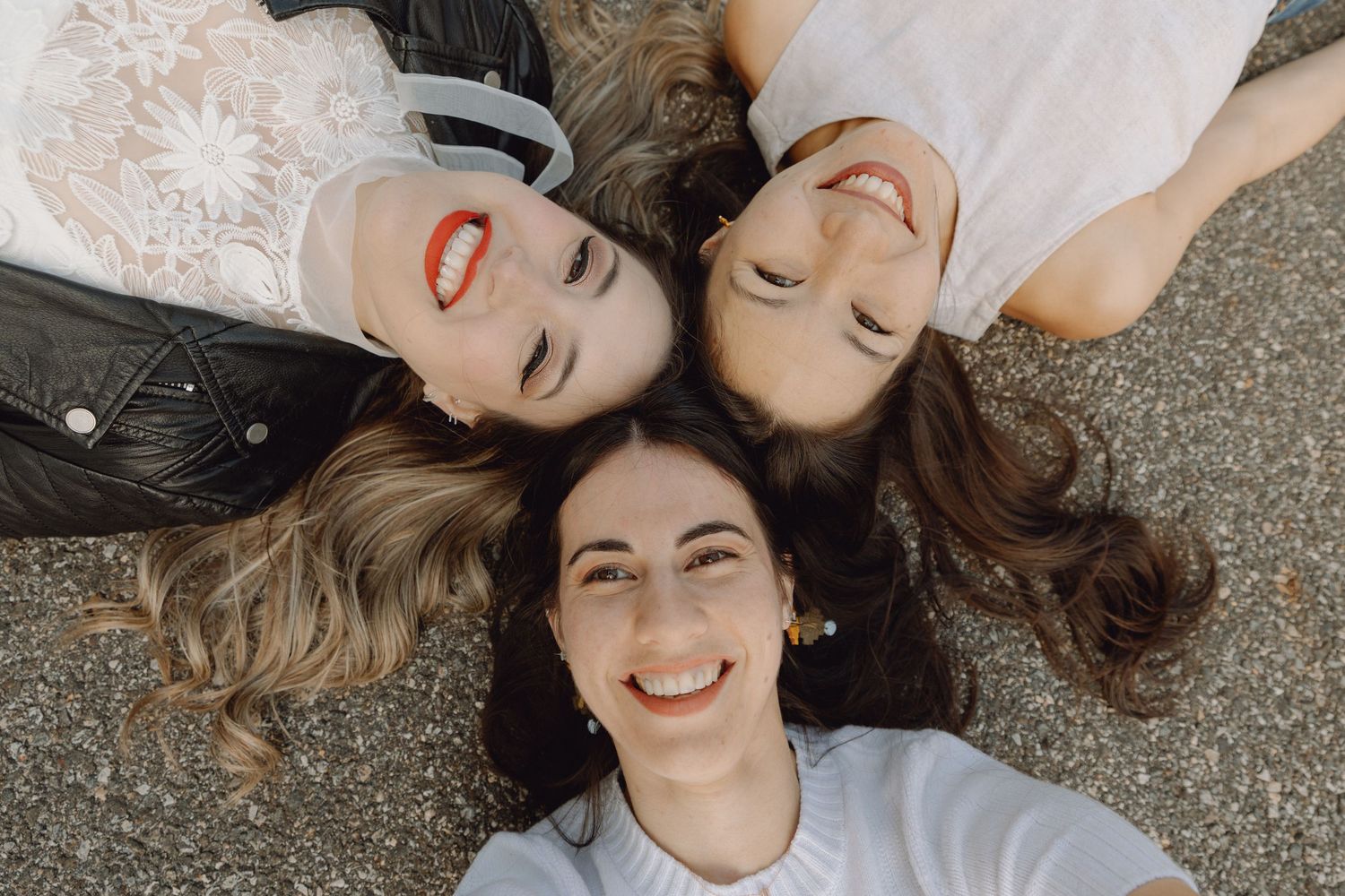 Three smiling women lying on the ground in a circle, viewed from above.