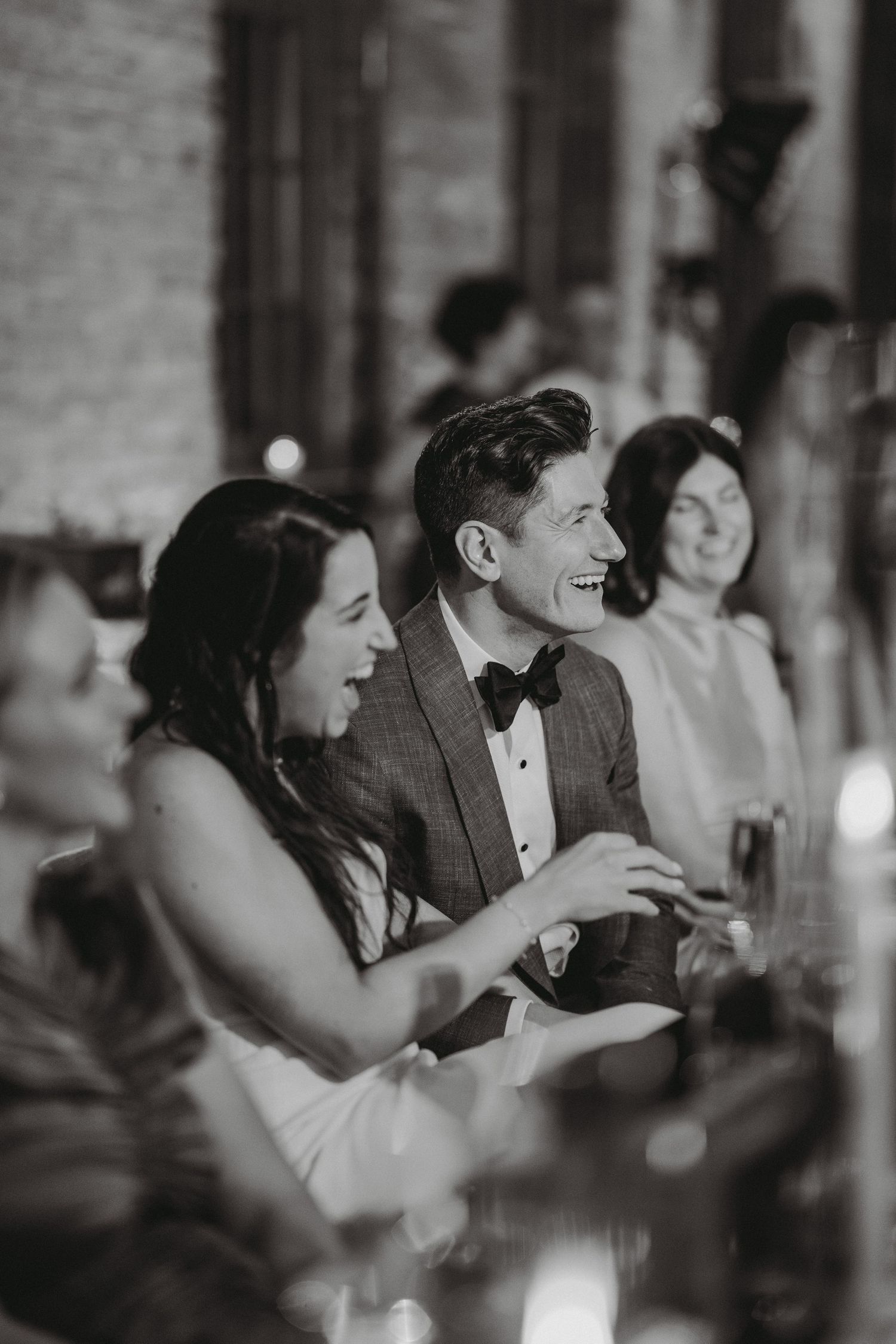 Bride and groom laugh joyfully during wedding reception speeches.
