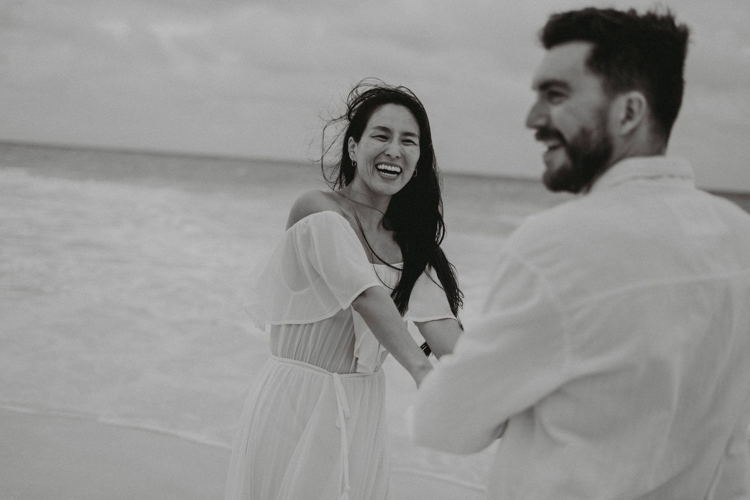 Black and white photo of a couple smiling and laughing together on a breezy beach.