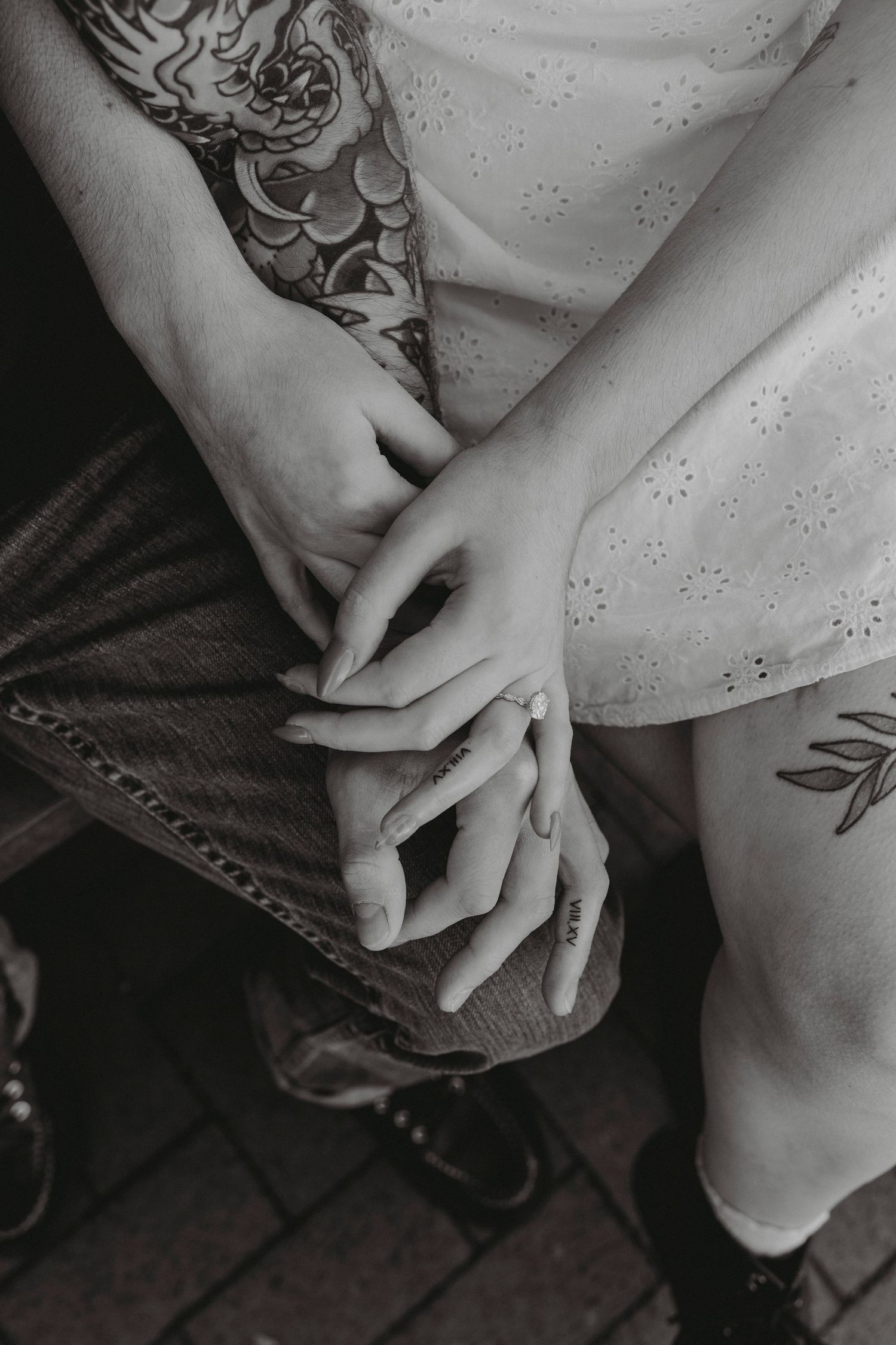 Black and white close-up of a couple holding hands, showcasing intricate tattoos on their arms.