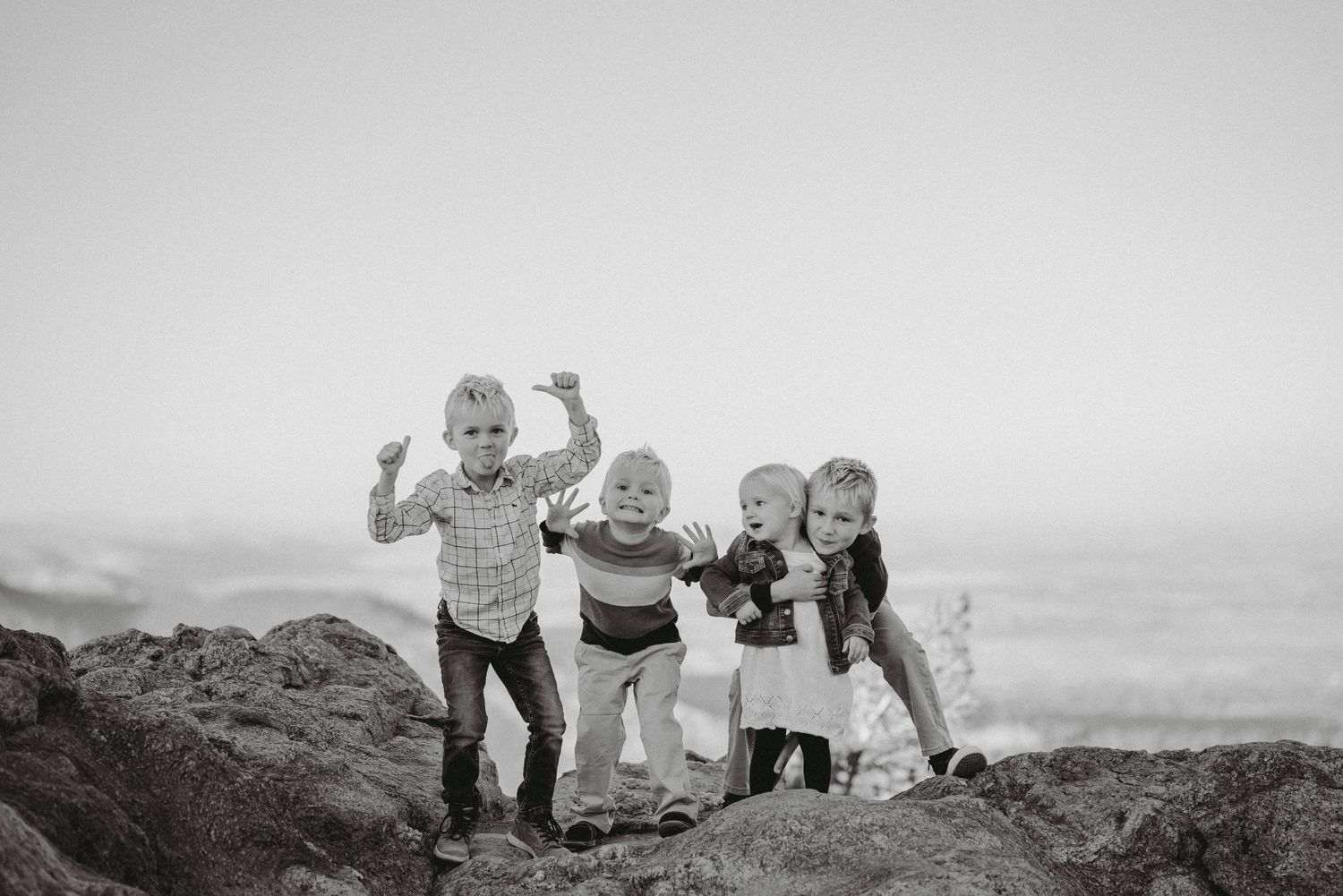 Black and white photo of four young children posing playfully on rocks with a scenic landscape behind.