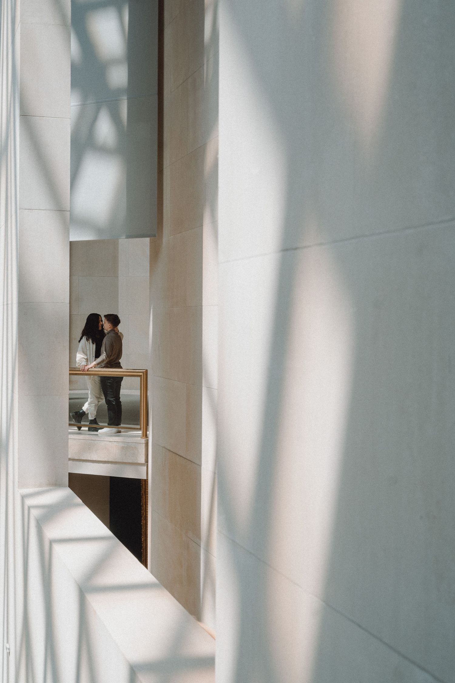 Couple sharing a tender moment framed by sunlit architectural columns and soft shadows.