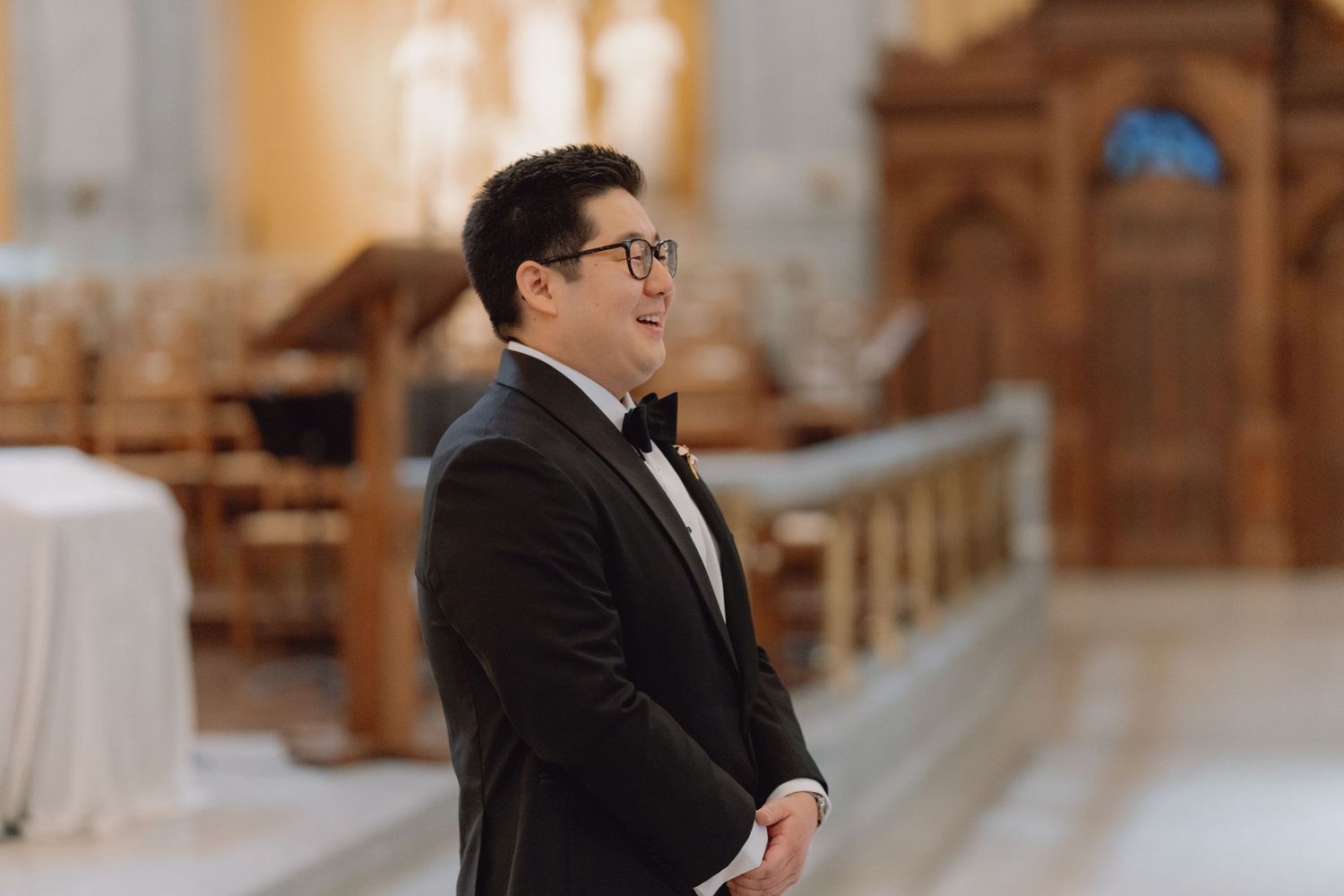 Groom in black tuxedo standing at church altar awaiting bride during wedding ceremony.