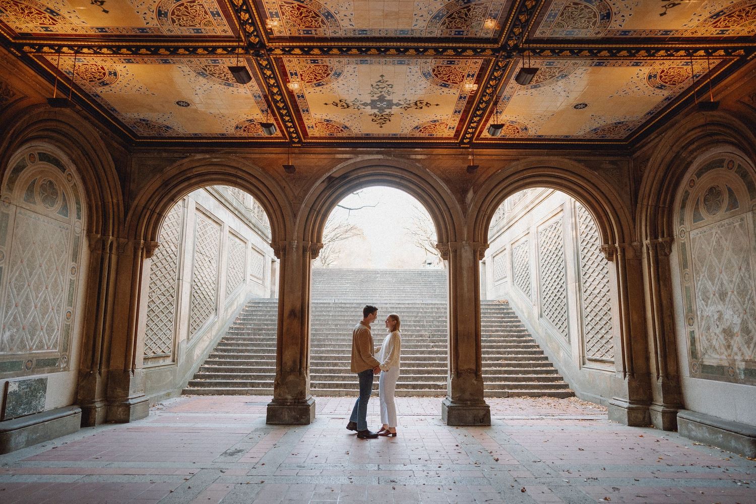 Couple standing together under ornate arched architecture at Bethesda Terrace in Central Park, NYC.