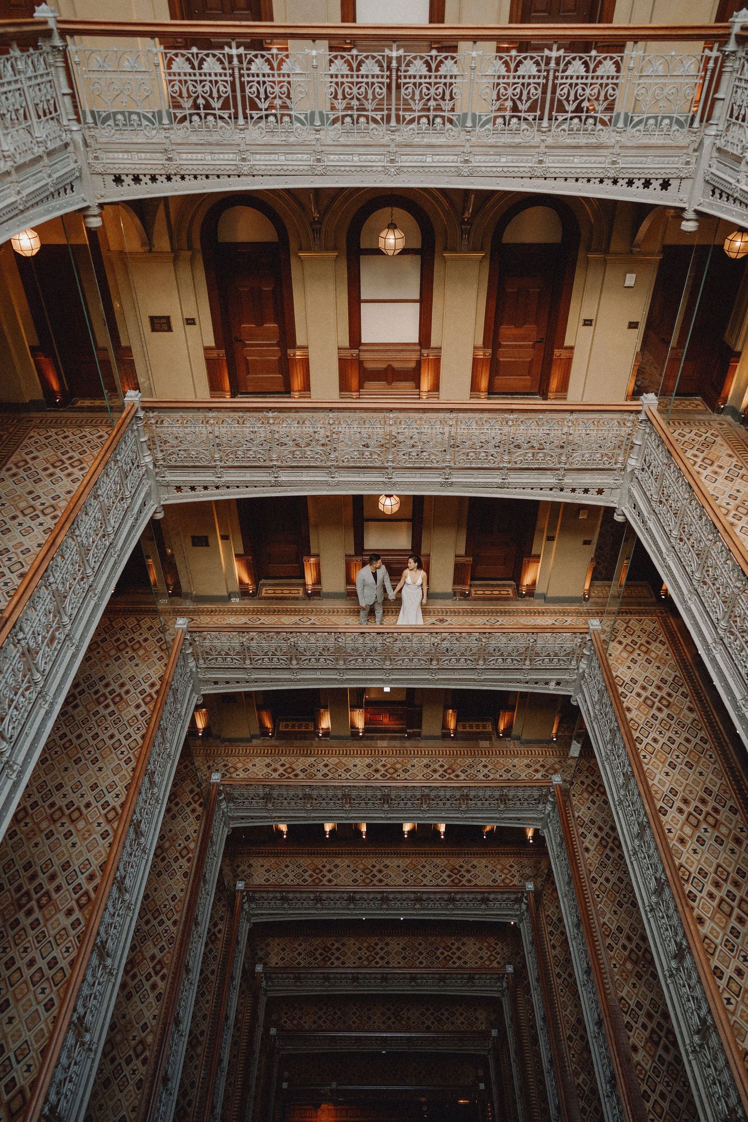 Dramatic wide-angle view of couple standing on balcony inside a stunning multi-story historic atrium.