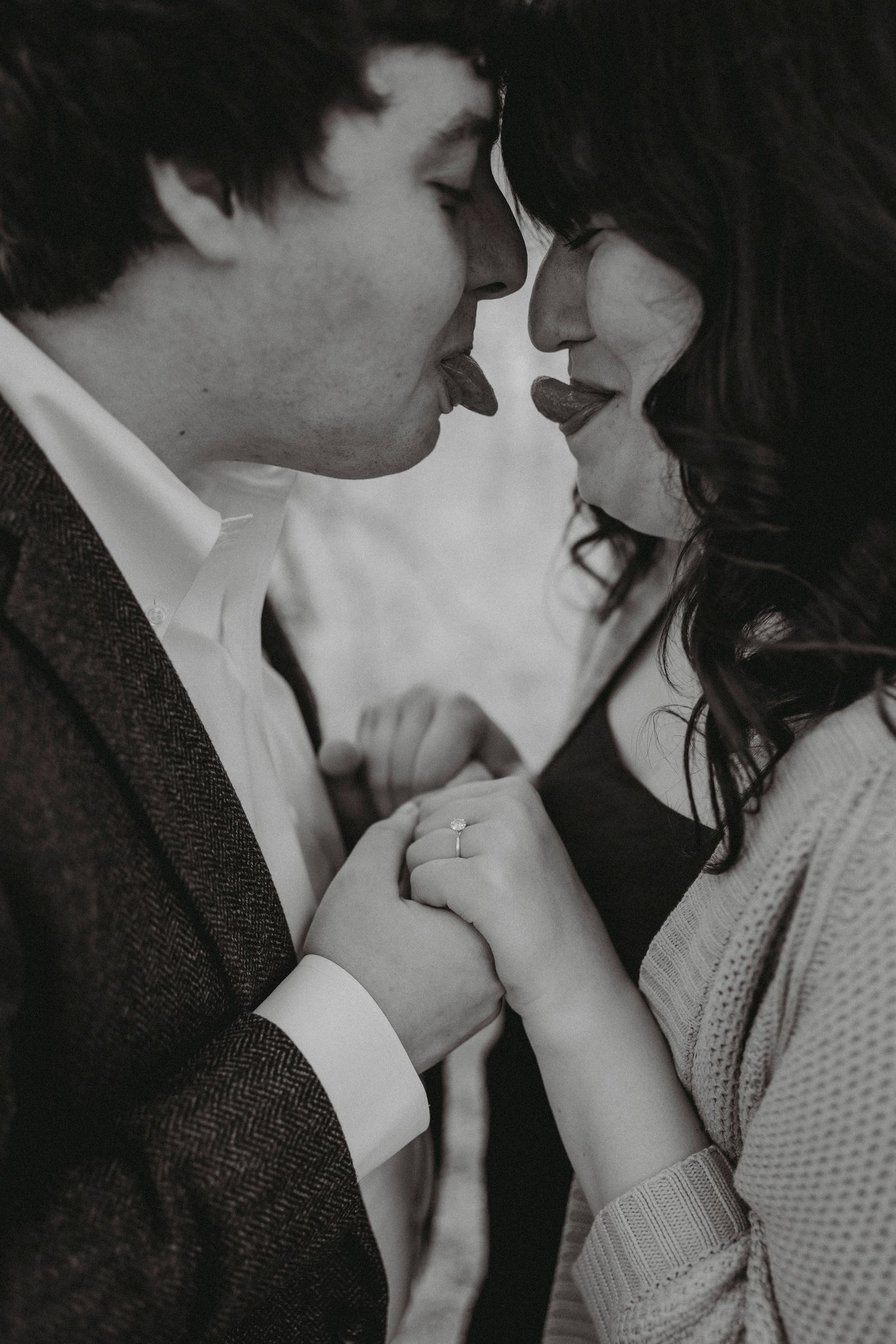 Black and white intimate close-up of an engaged couple nearly kissing while holding hands.