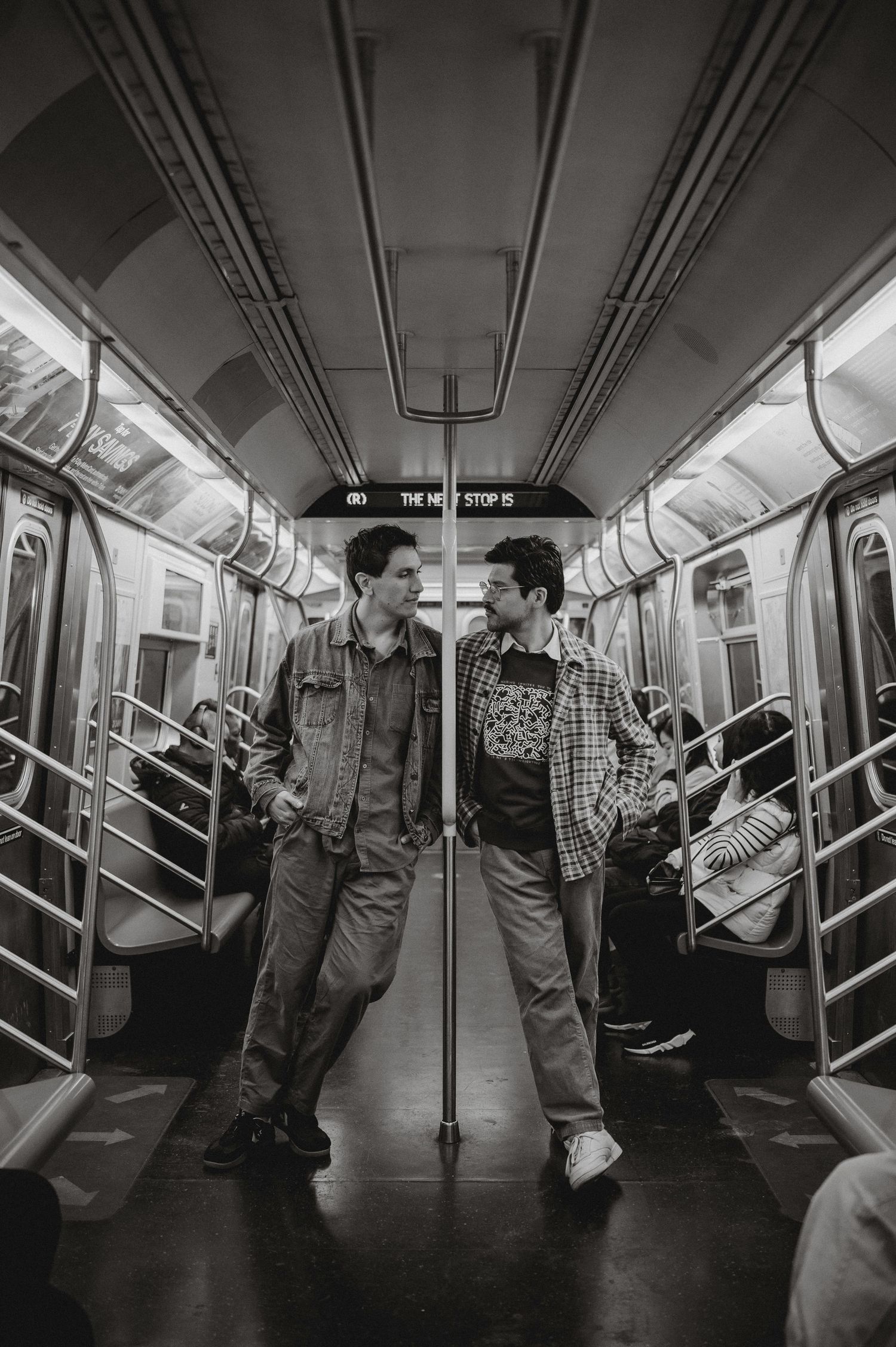 Two men stand facing each other in an empty New York City subway car in black and white.