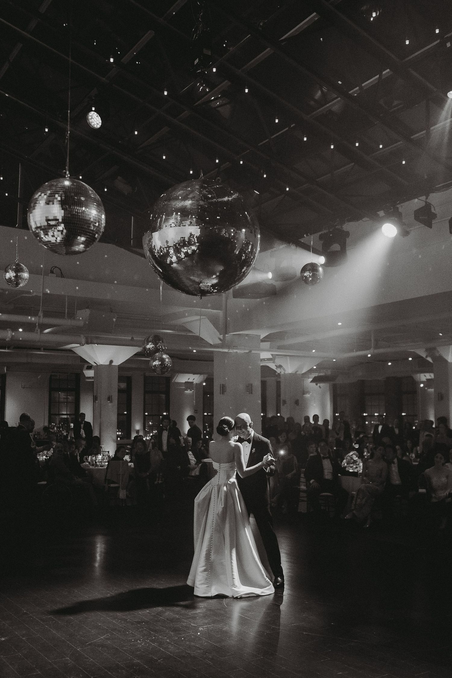 Bride and groom share first dance under sparkling disco balls in elegant black and white wedding reception photo.