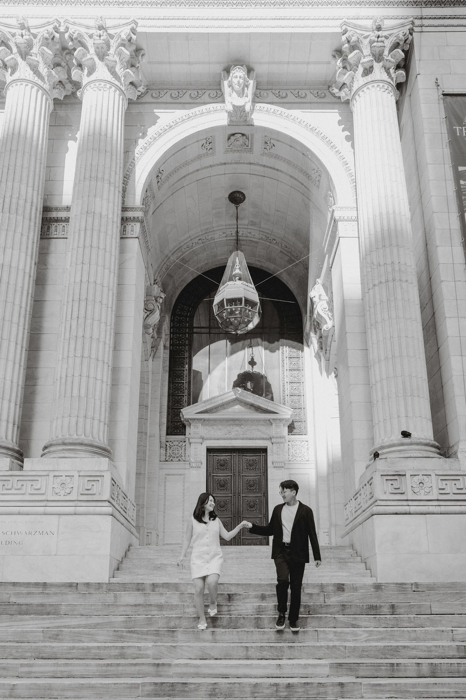 Black and white photo of couple descending steps of a grand neoclassical building with tall Corinthian columns.