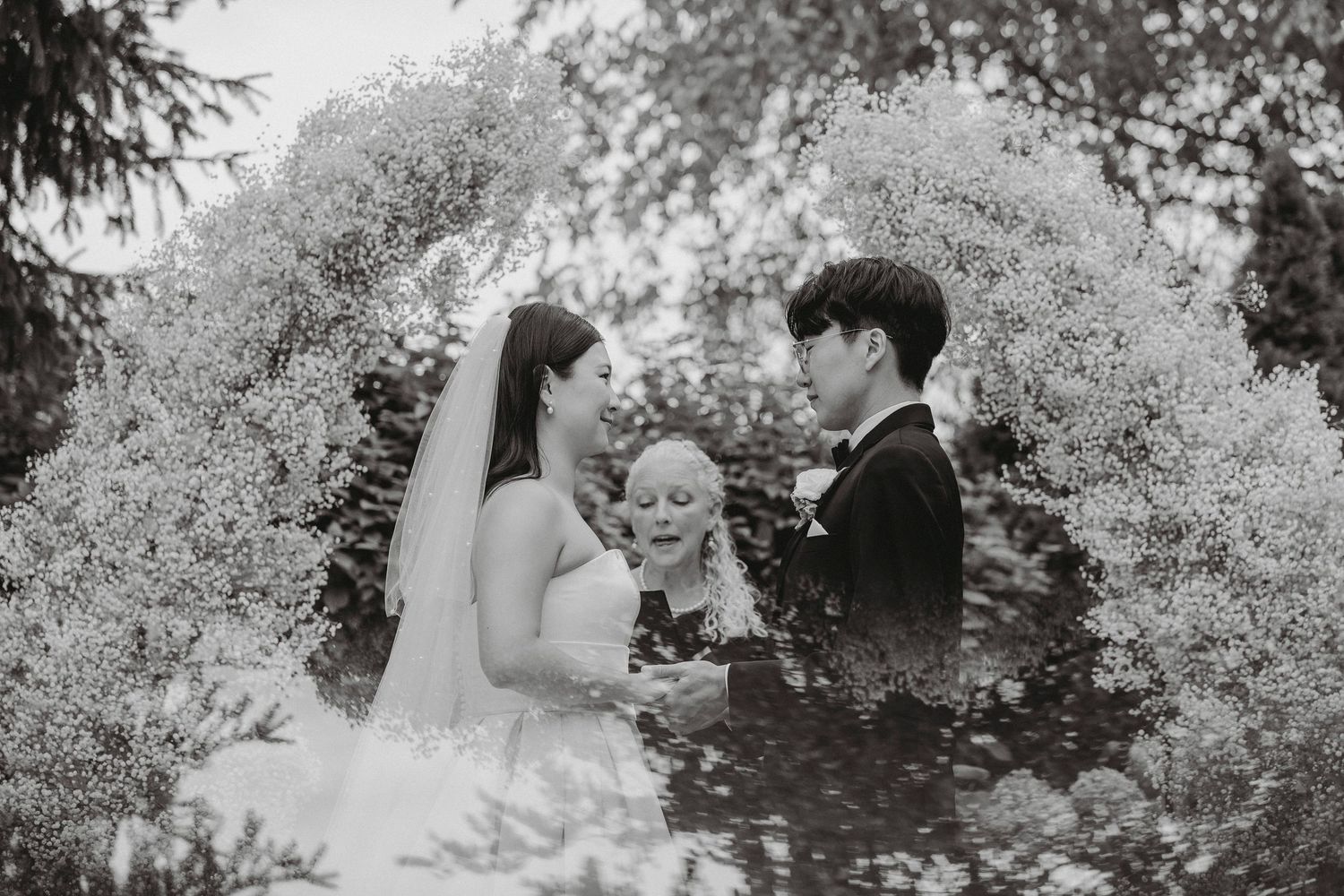 Bride and groom exchange vows under floral arch with officiant at outdoor wedding ceremony.