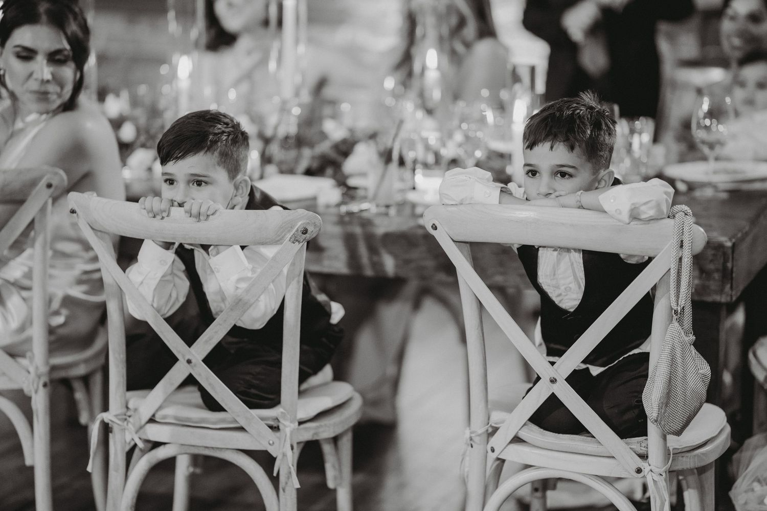 Two young ring bearers lean on chairs at wedding reception dinner table.