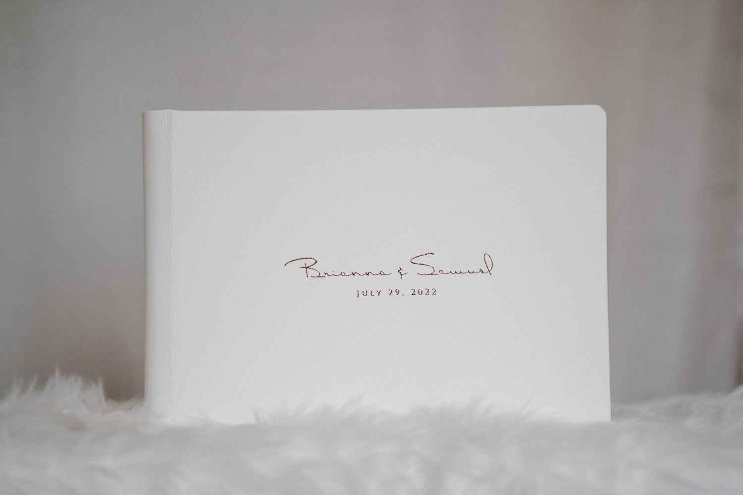 Minimalist white wedding album with romantic red cursive script names and wedding date on cover.
