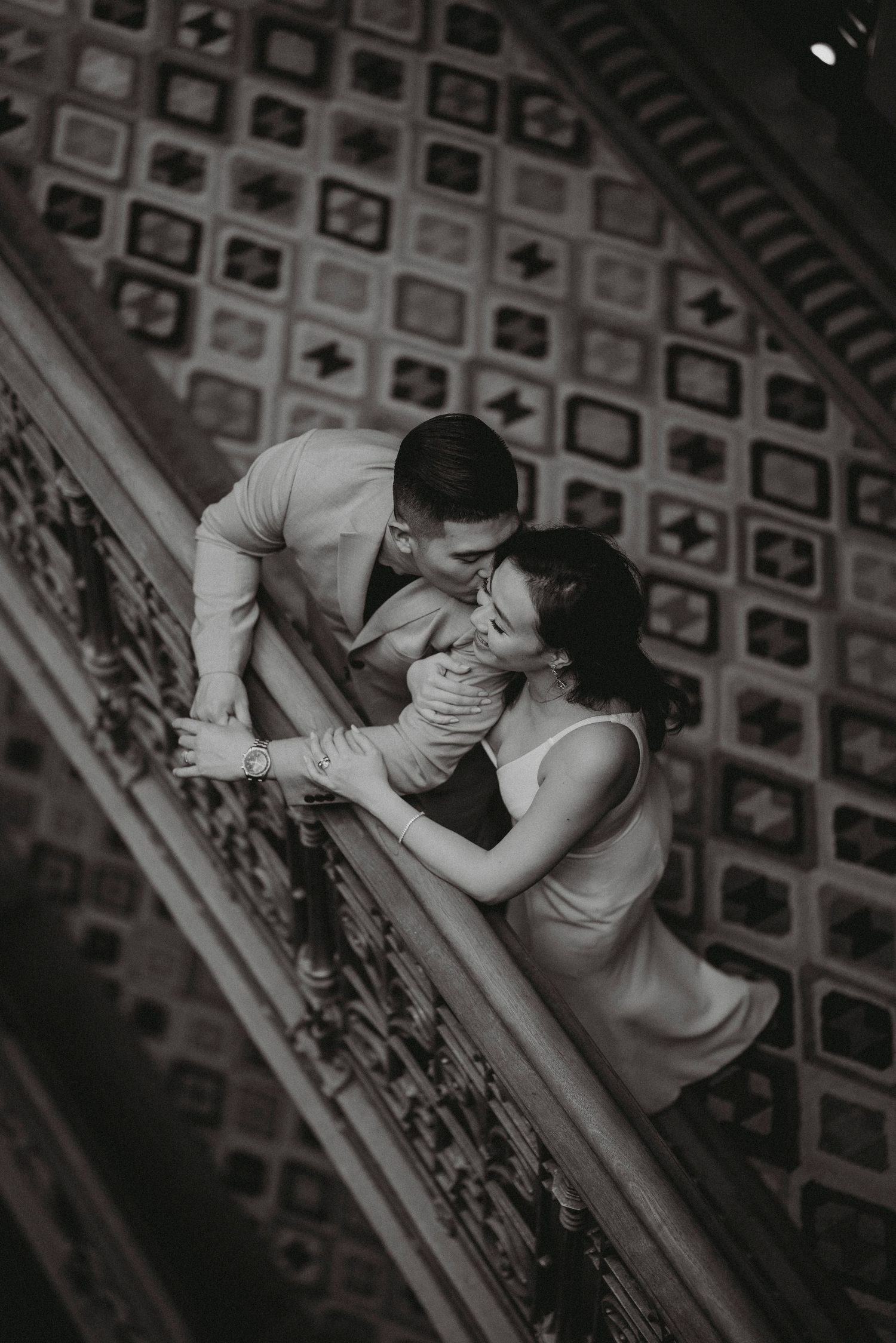 Black and white overhead shot of couple sharing a romantic moment on an ornate staircase.