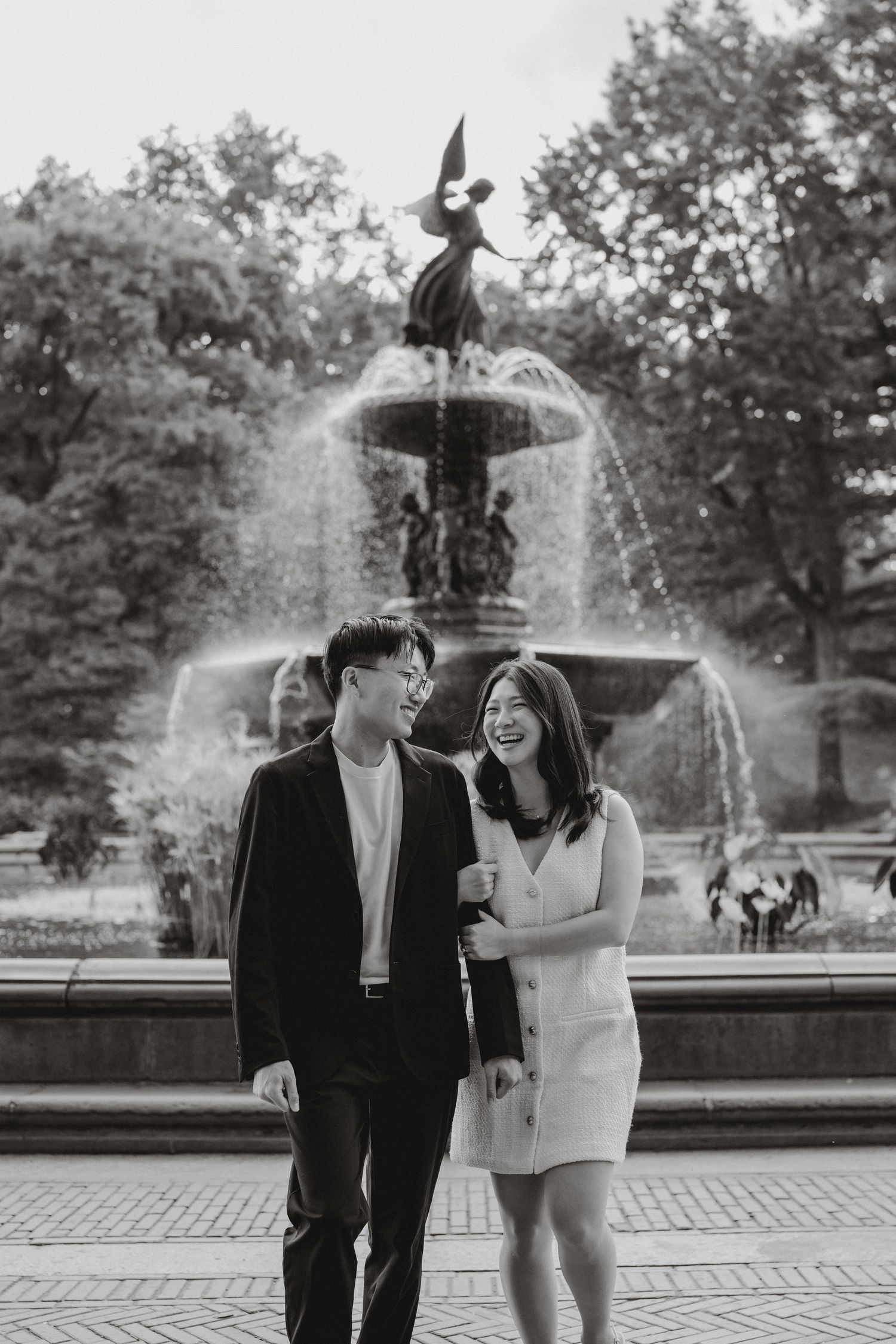Laughing couple strolls together in front of Bethesda Fountain in Central Park engagement session.