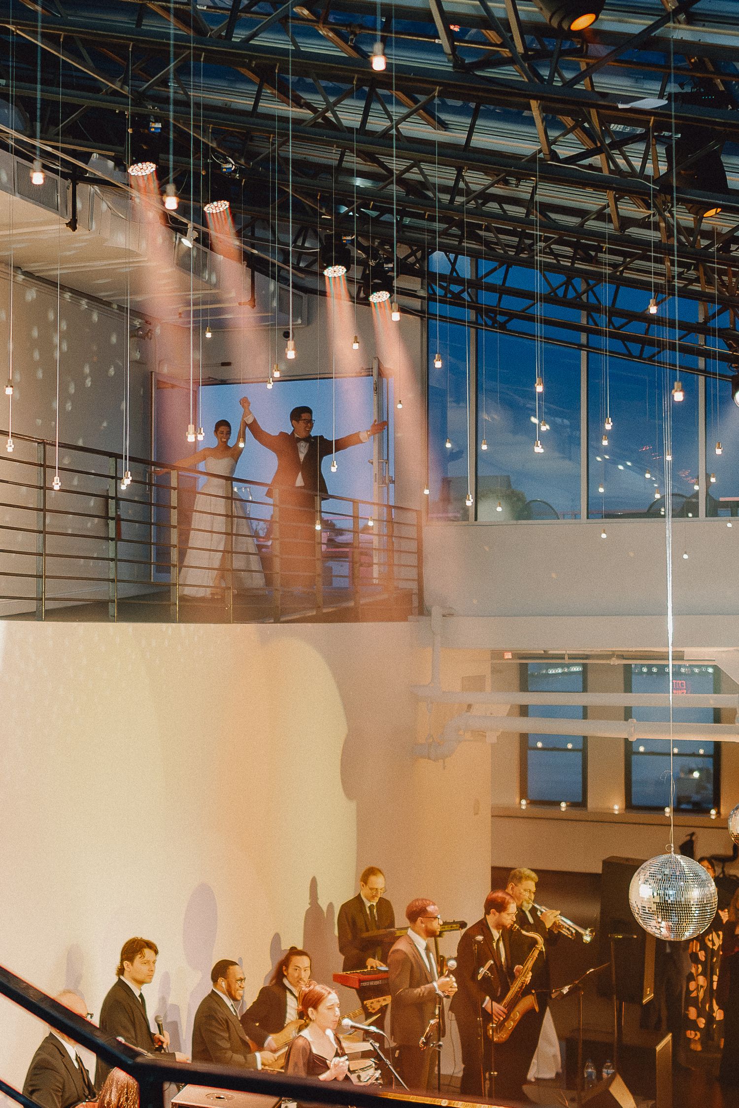 Live jazz band performs below a mezzanine where guests dance at an elegant evening wedding reception venue.