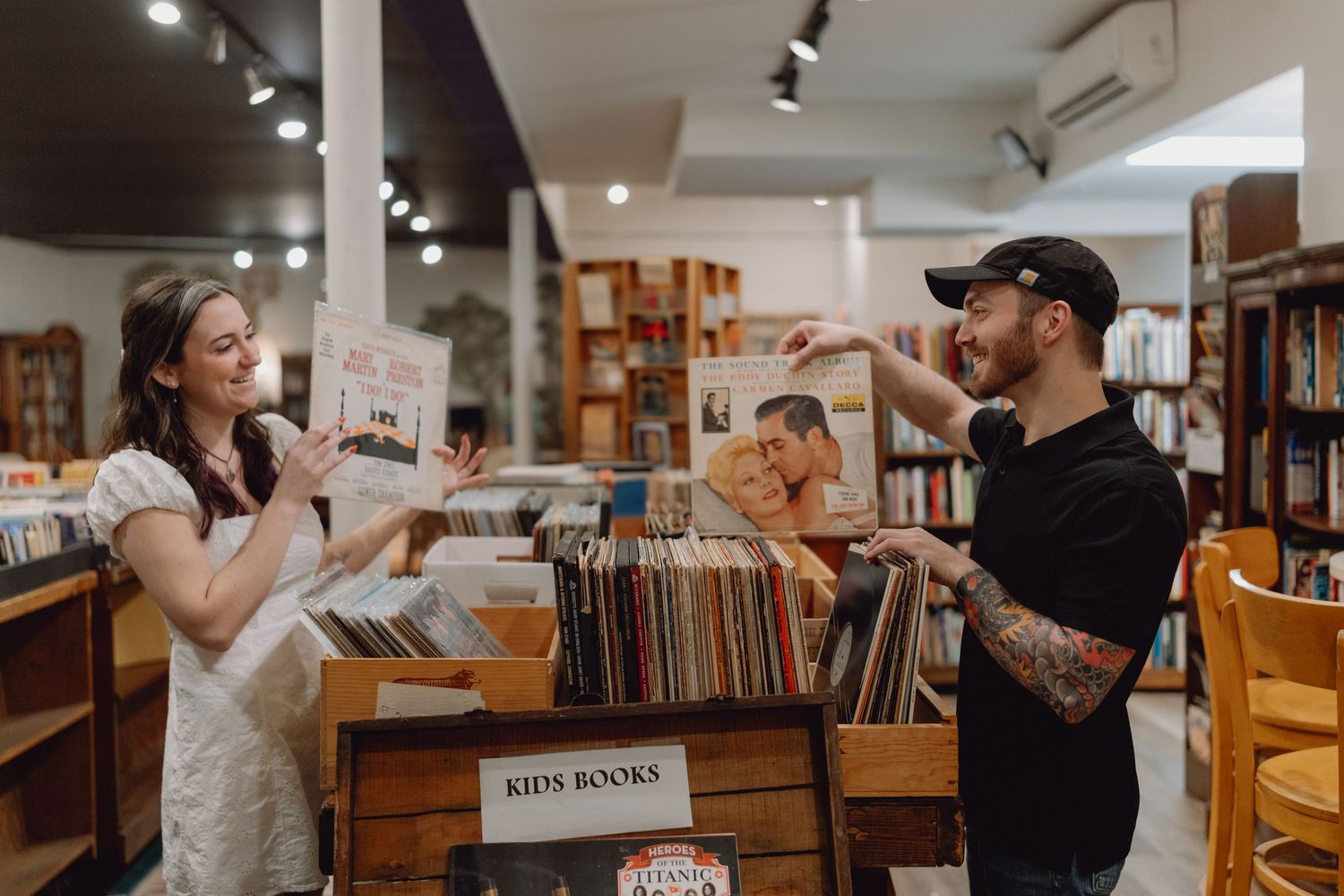 Couple browsing vinyl records and books at an indie record store, sharing a joyful moment together.