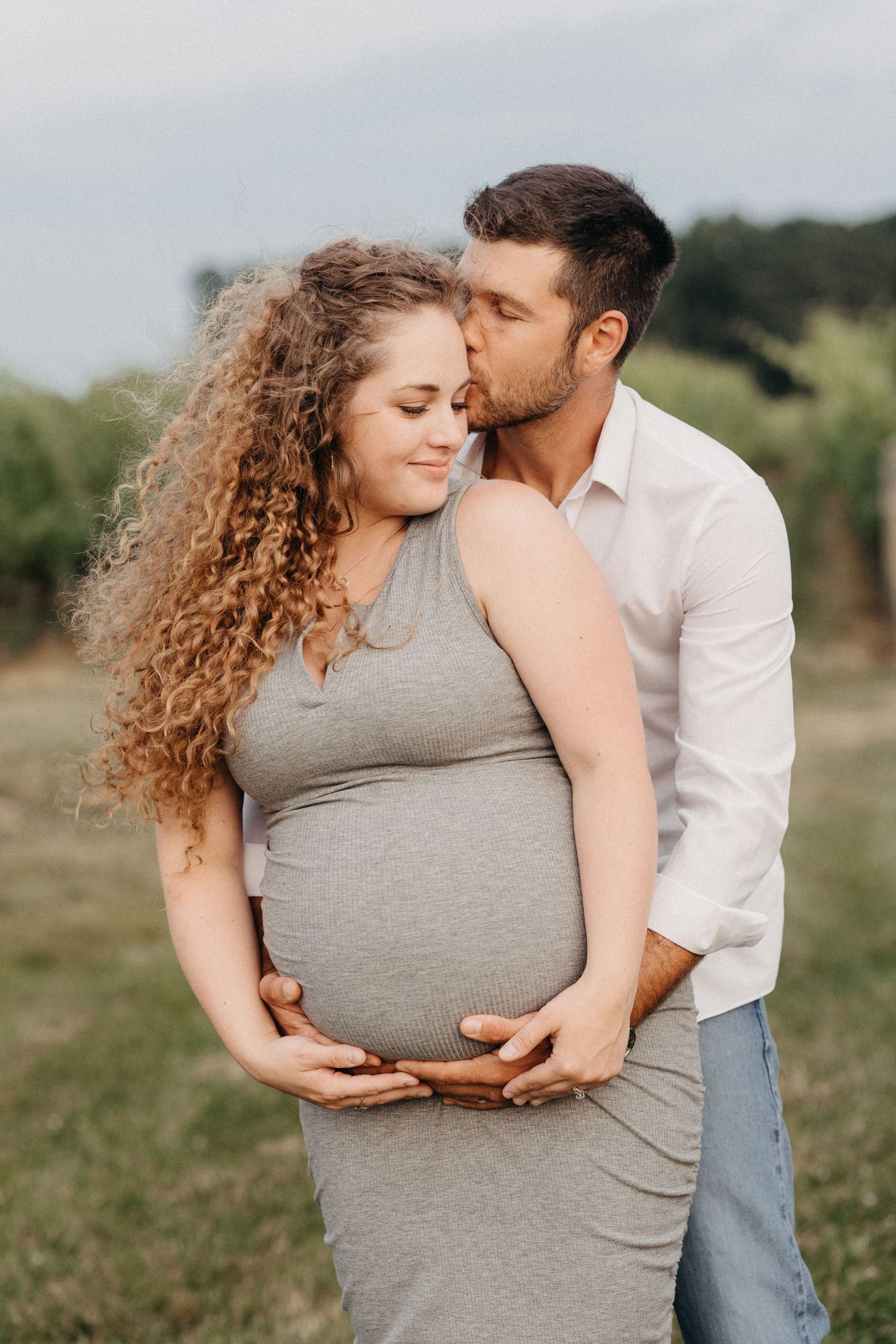 Man kissing pregnant woman with curly hair outdoors.