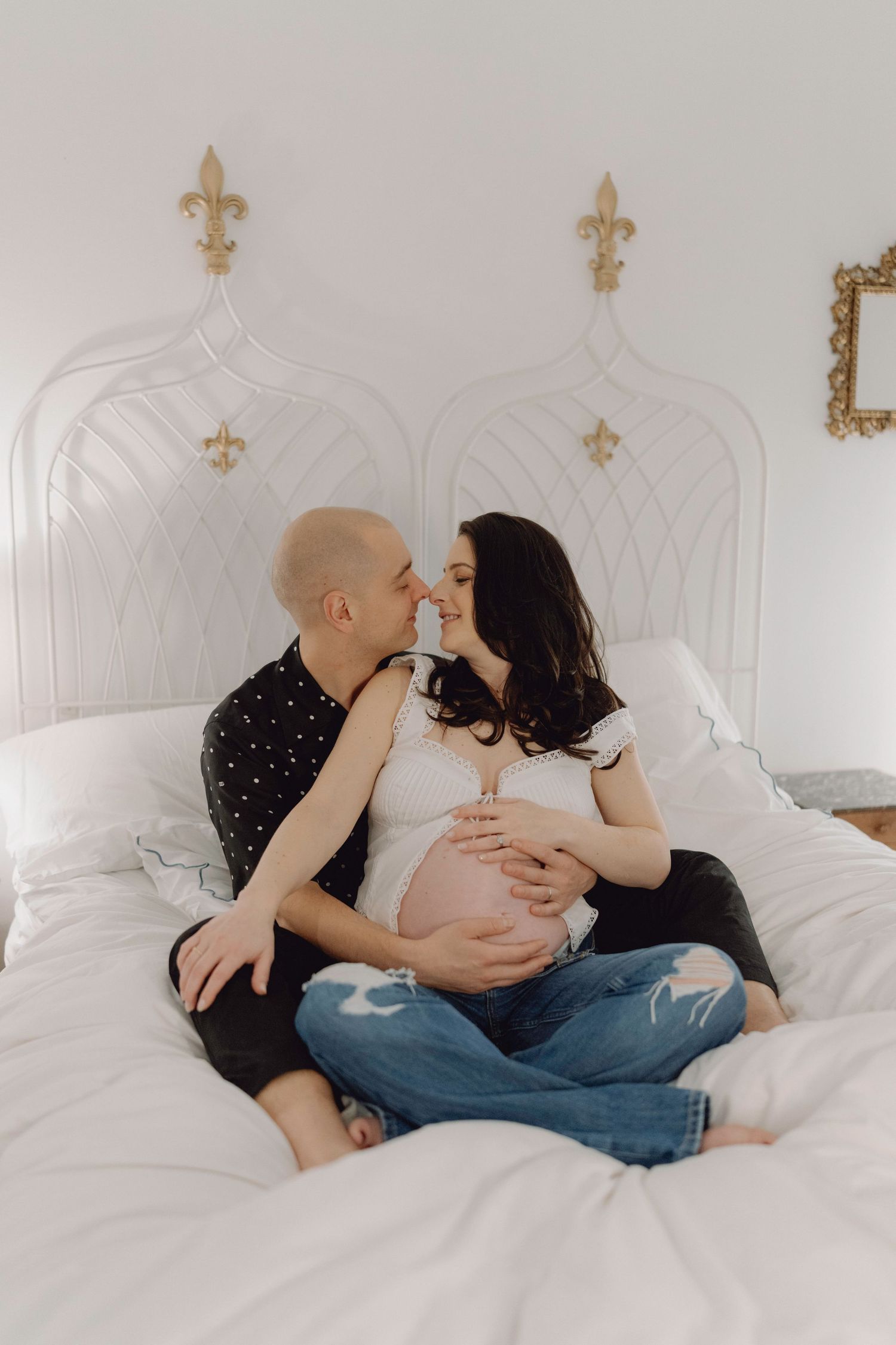 Couple kissing on bed with pregnant belly showing.