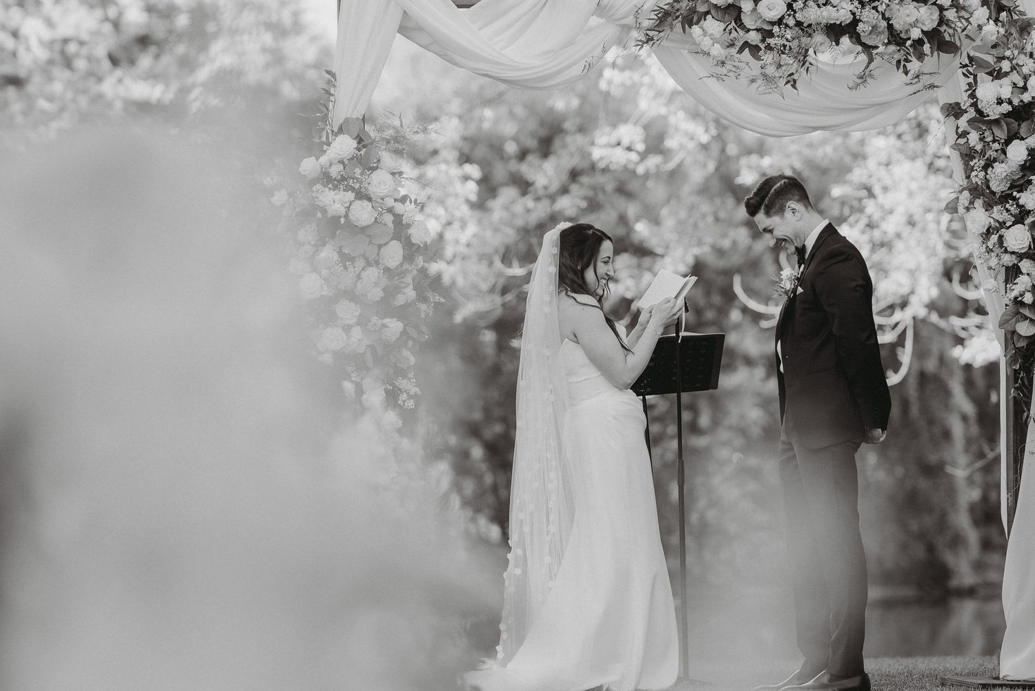 Bride and groom exchange rings under floral wedding arch outdoors.