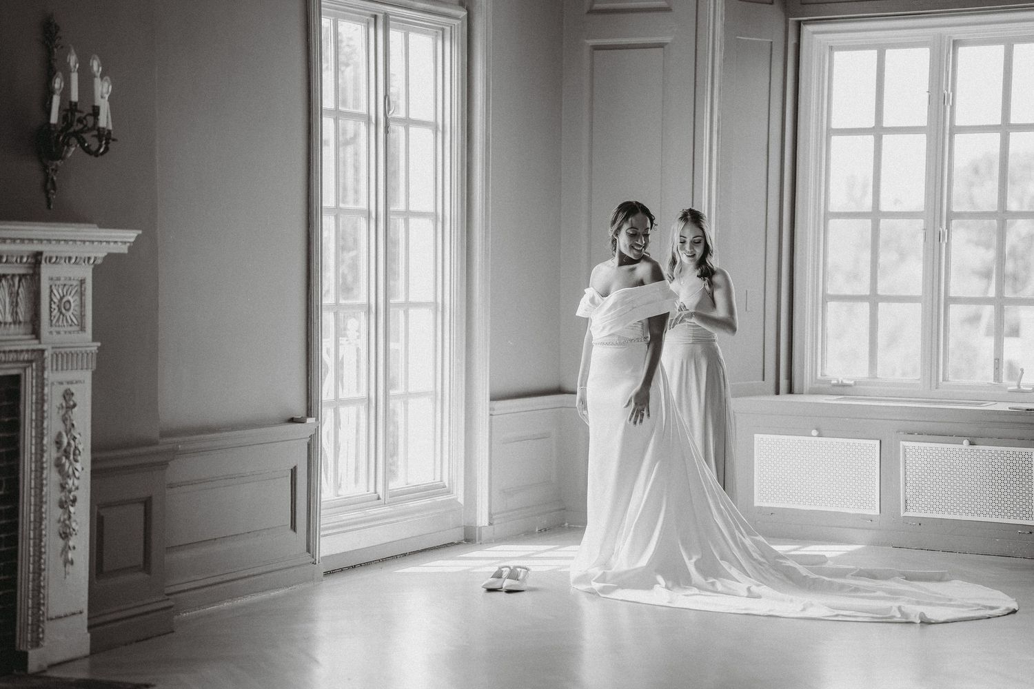 Black and white photo of bride and bridesmaid sharing vows in elegant white ballroom.