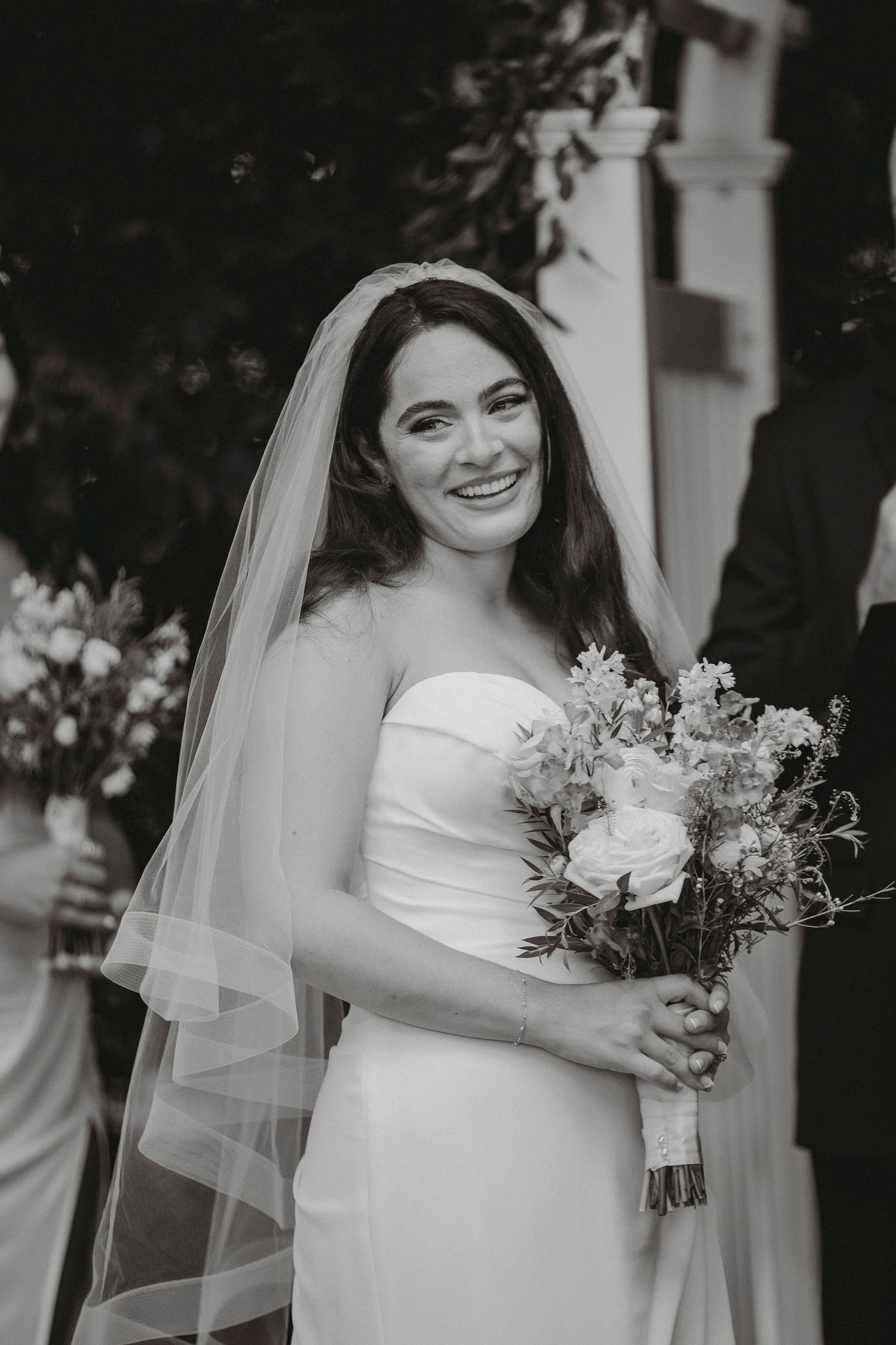 Black and white portrait of smiling bride holding bouquet in strapless gown and veil.