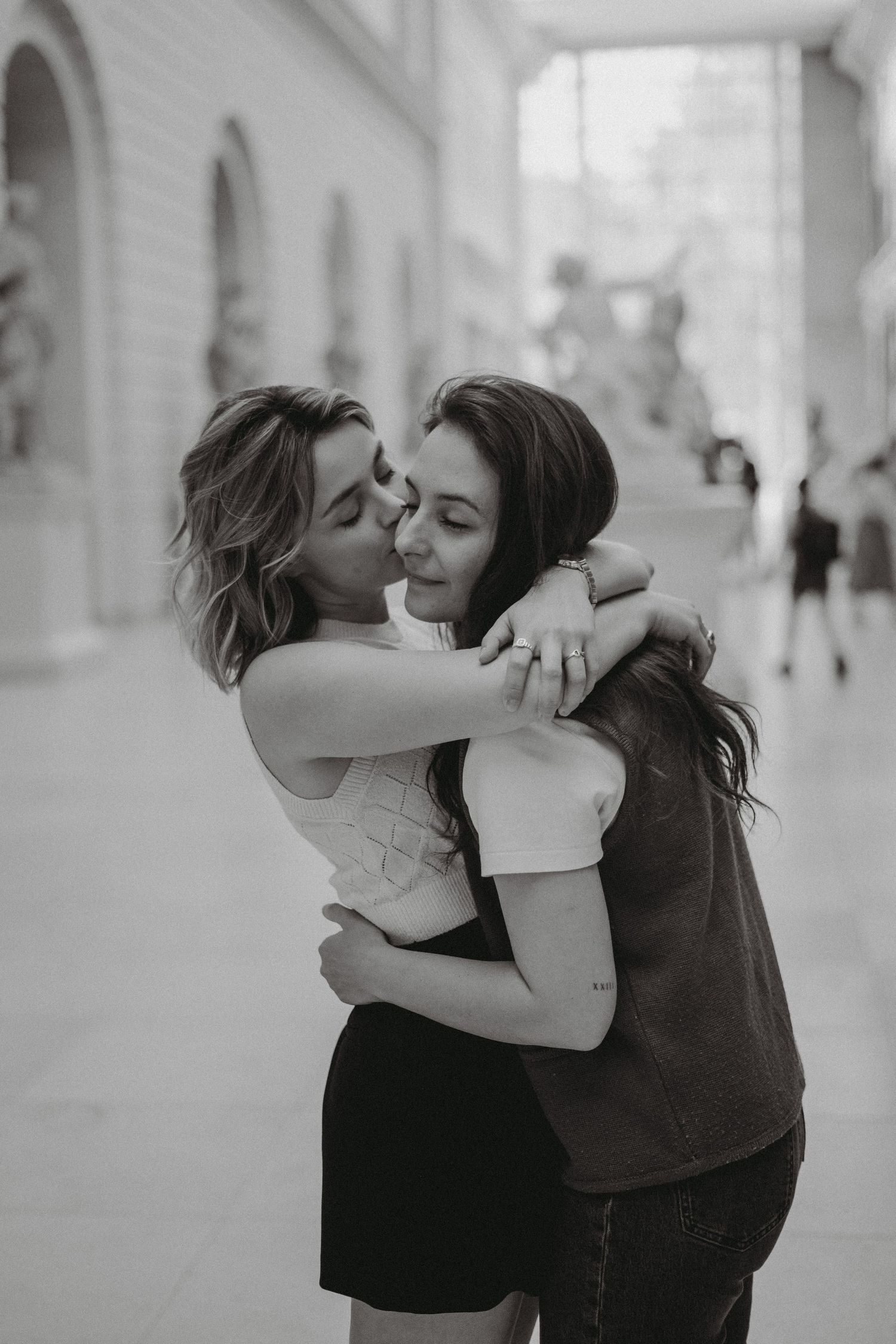 Two women share a warm embrace outdoors in a black and white couples portrait photo.