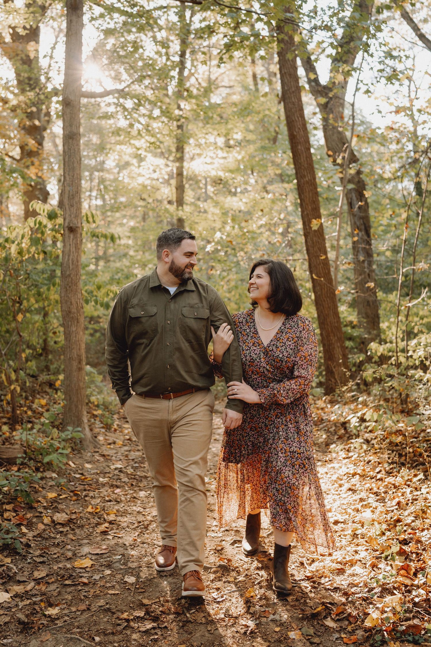Happy couple walking together on a leaf-covered forest trail during golden autumn season.