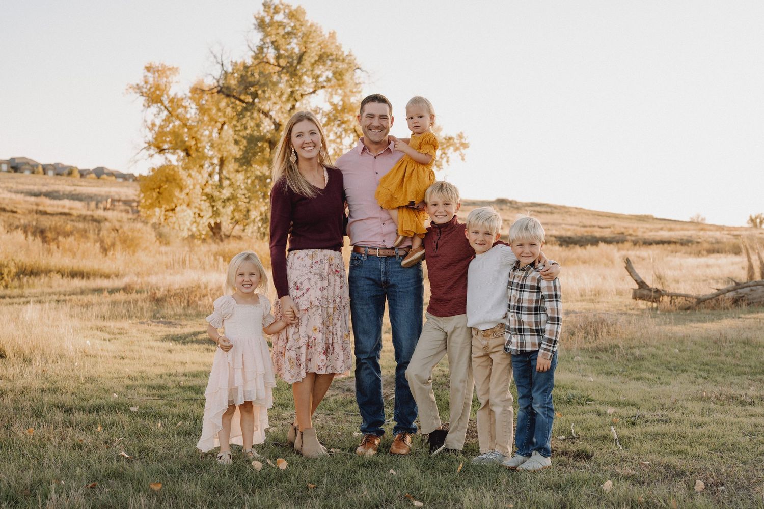 Family of six smiling together in a golden autumn field at sunset.