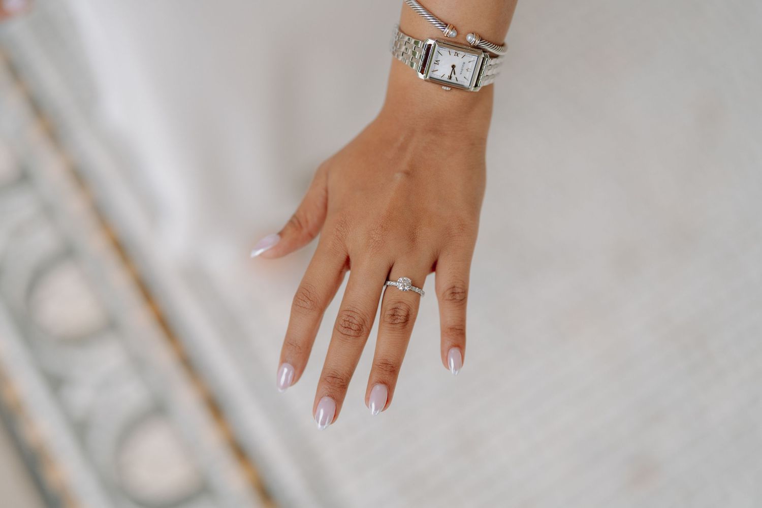 Close-up of a bride's hand displaying a diamond engagement ring with French tip nails and a watch.