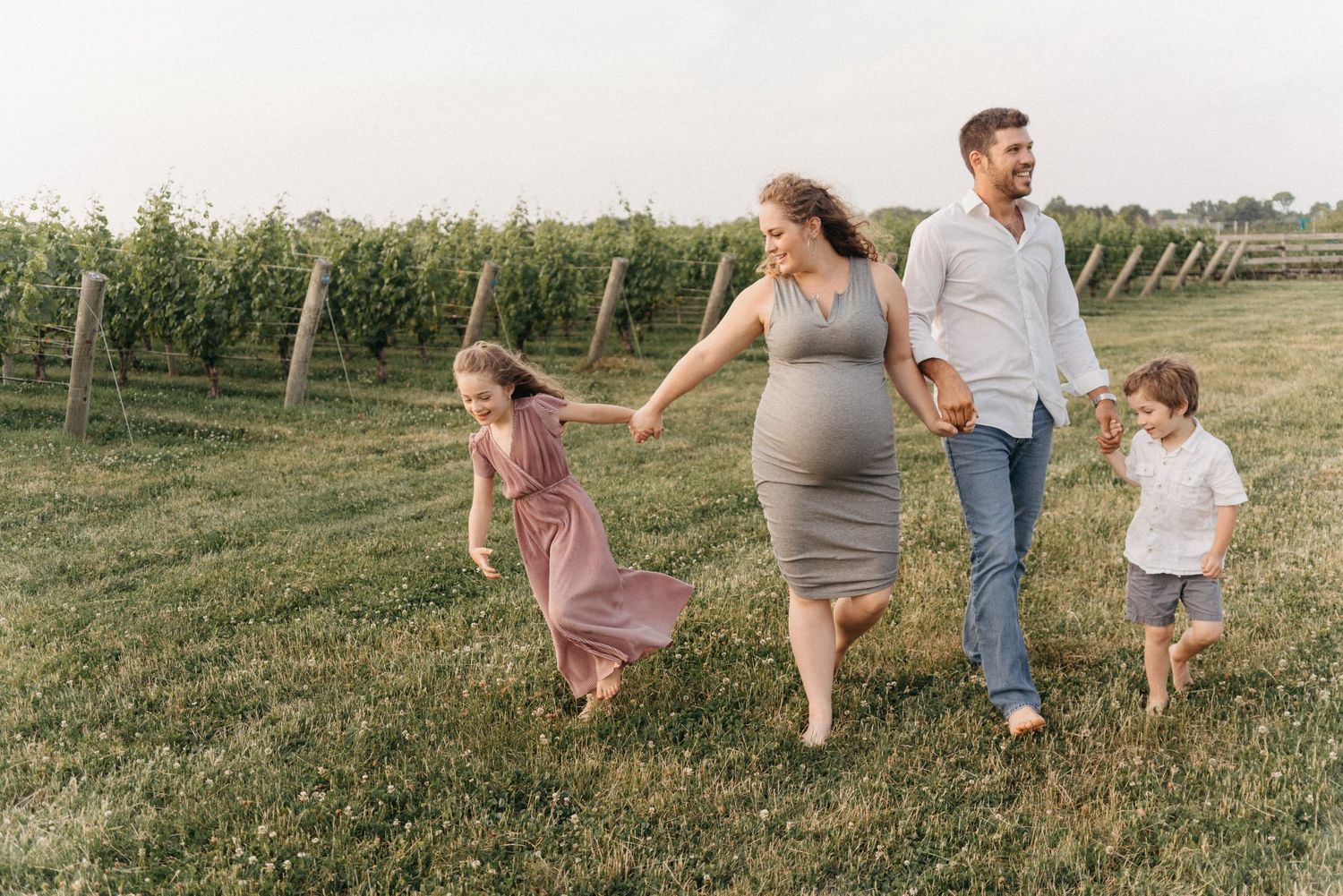 Pregnant woman walking with family in vineyard field.