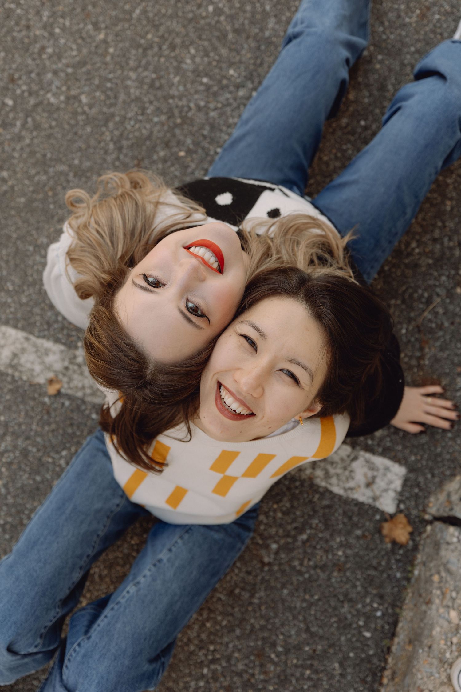 Aerial view of two smiling women lying on pavement with heads together looking up at camera.