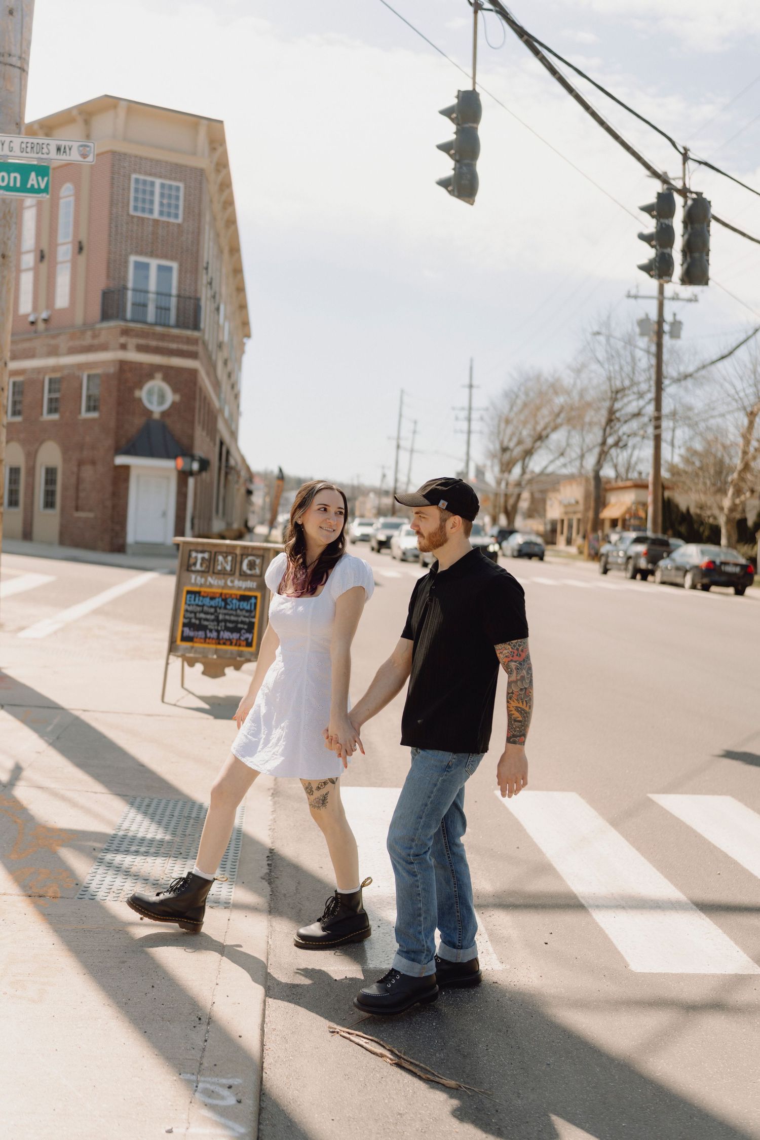 Young couple holding hands while crossing a sunny street intersection in a casual urban neighborhood.