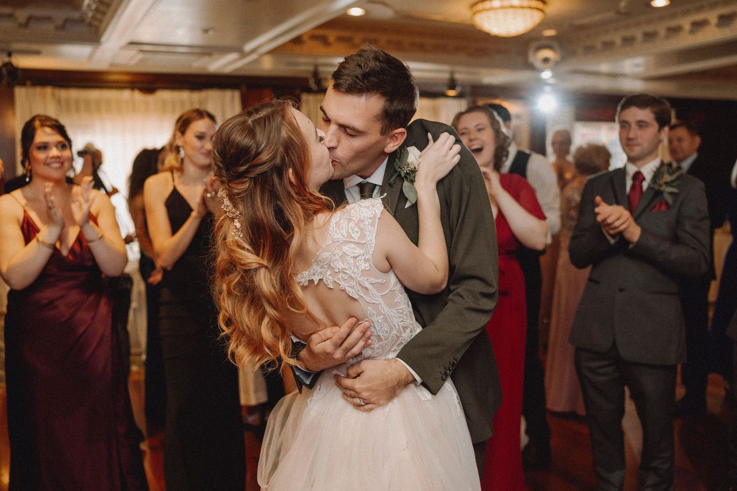 Bride and groom share their first dance kiss surrounded by applauding guests at a wedding reception.