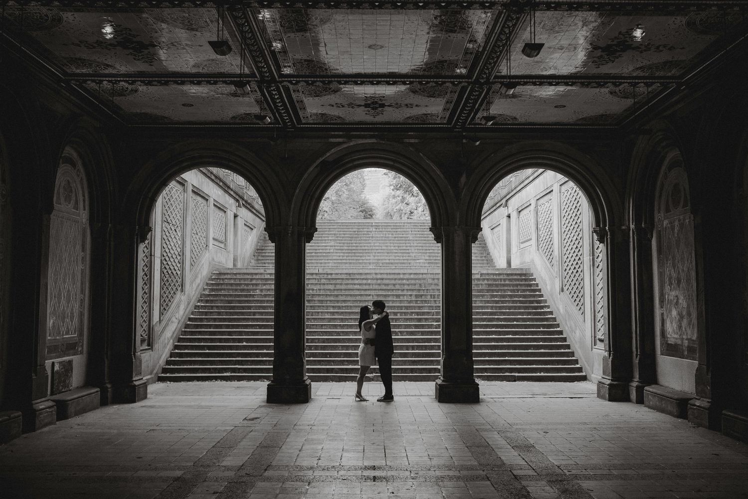 Couple shares romantic kiss silhouetted under ornate arches of Bethesda Terrace in Central Park.
