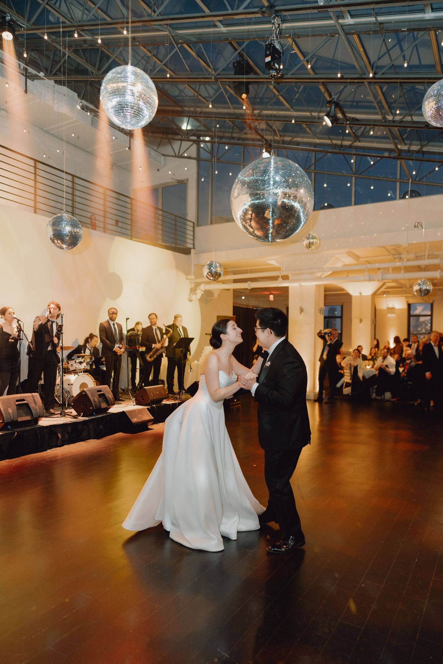 Bride and groom share first dance under sparkling disco balls in industrial chic wedding venue.